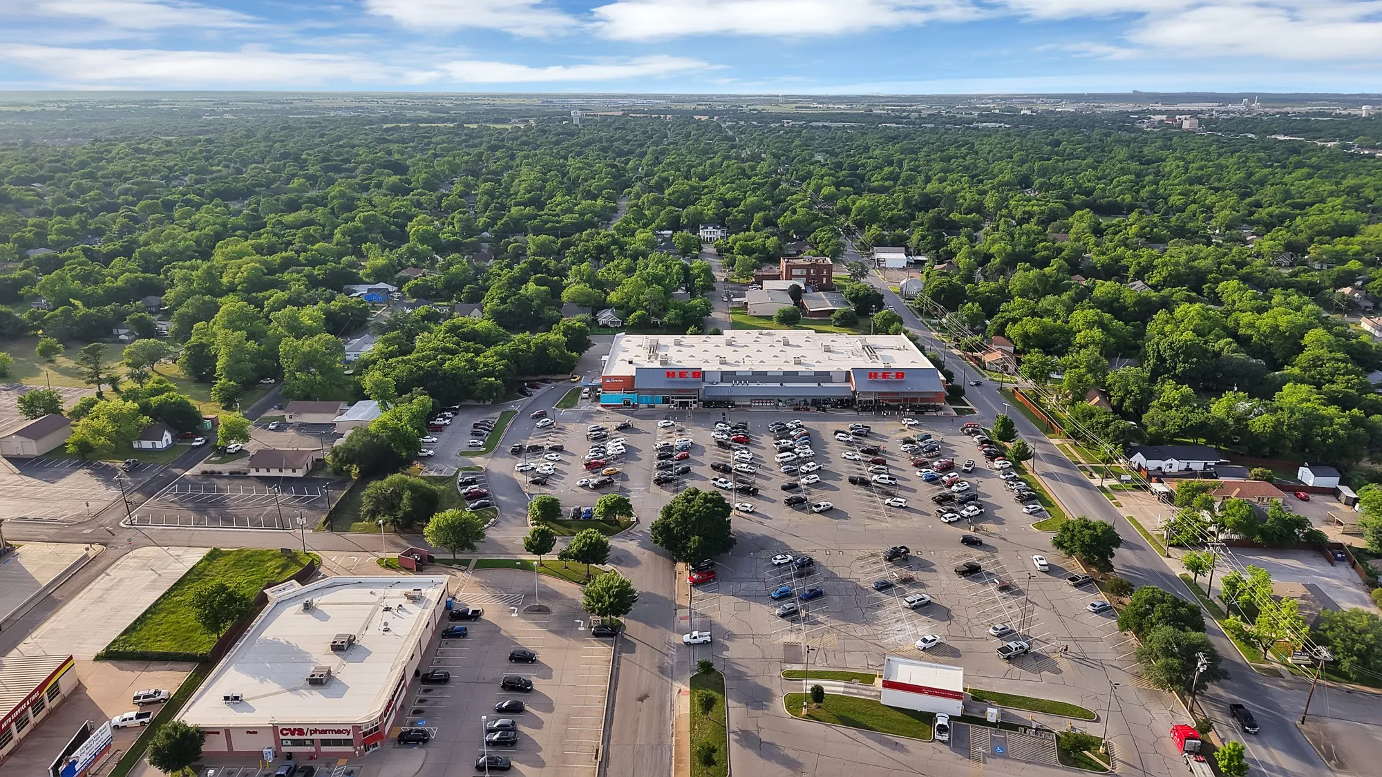 Aerial perspective showcasing a large commercial property with extensive parking, positioned within a tree-lined residential and commercial area