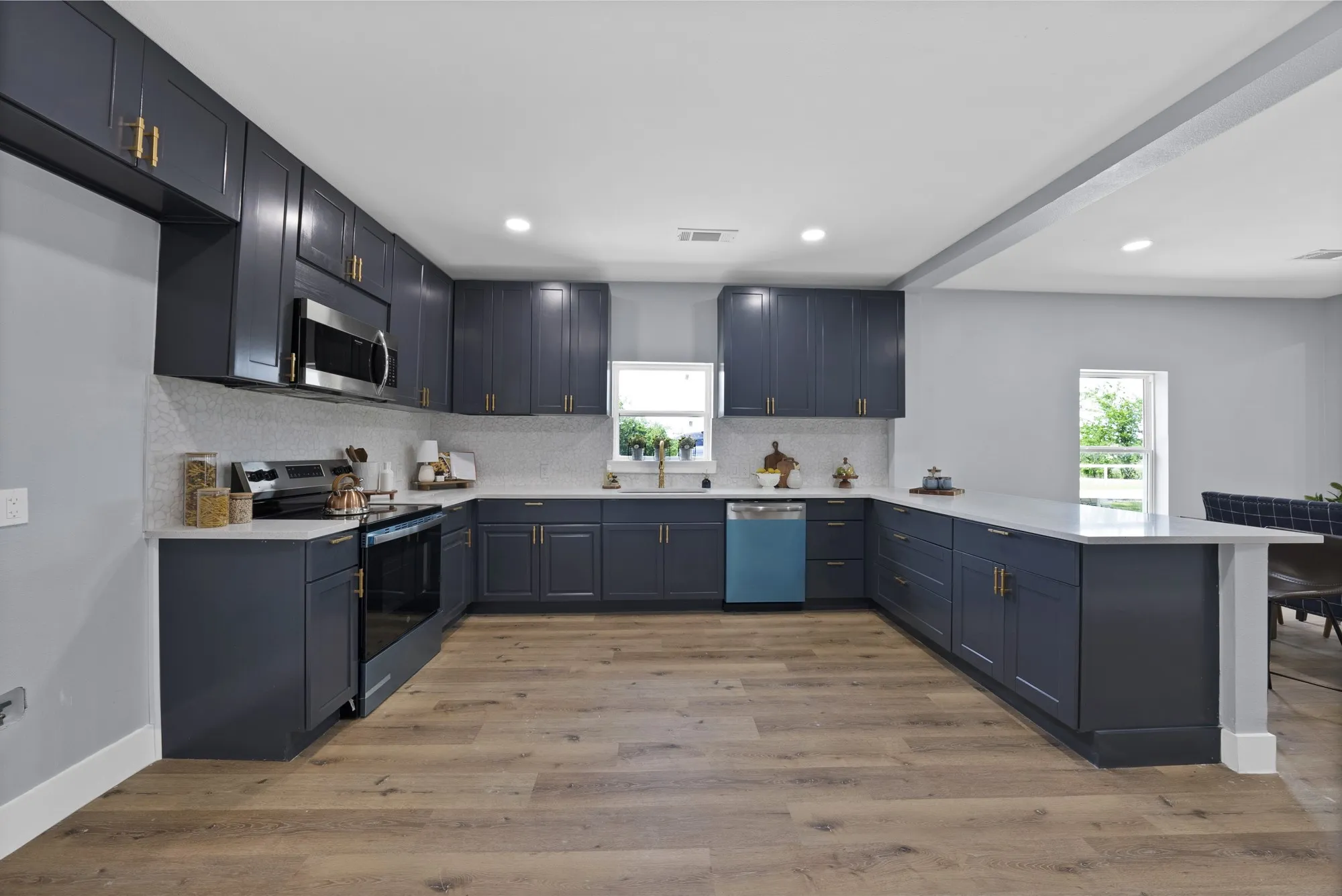 U-shaped kitchen featuring dark cabinetry with gold-tone hardware, stainless steel appliances, light countertops, and wood-finish flooring