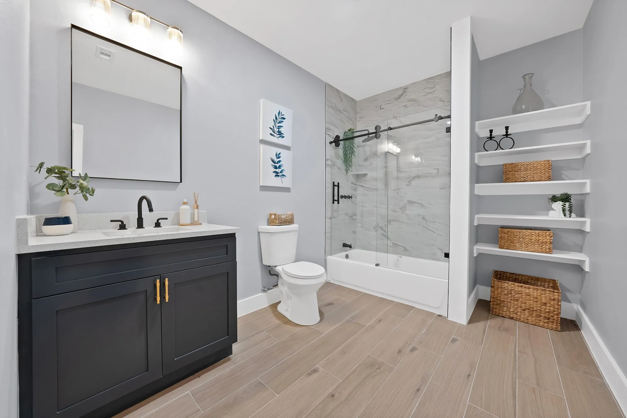 Bathroom featuring a dark wood-finish vanity with a light countertop, a rectangular mirror, a shower-tub combination with a sliding glass door and marble-look tile surround, and open shelving