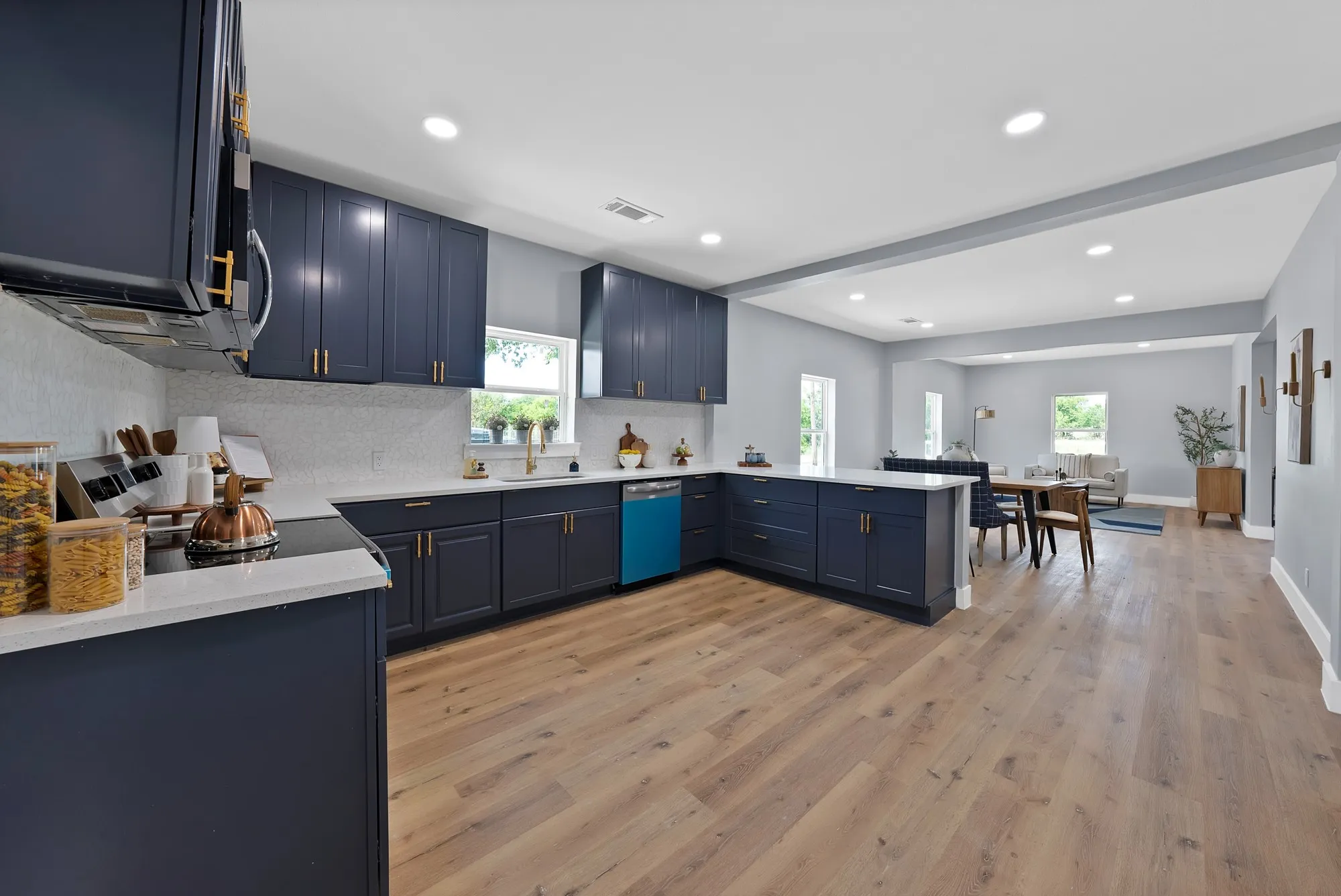 Contemporary kitchen featuring deep blue cabinetry with gold-tone hardware, white countertops, and a white mosaic tile backsplash