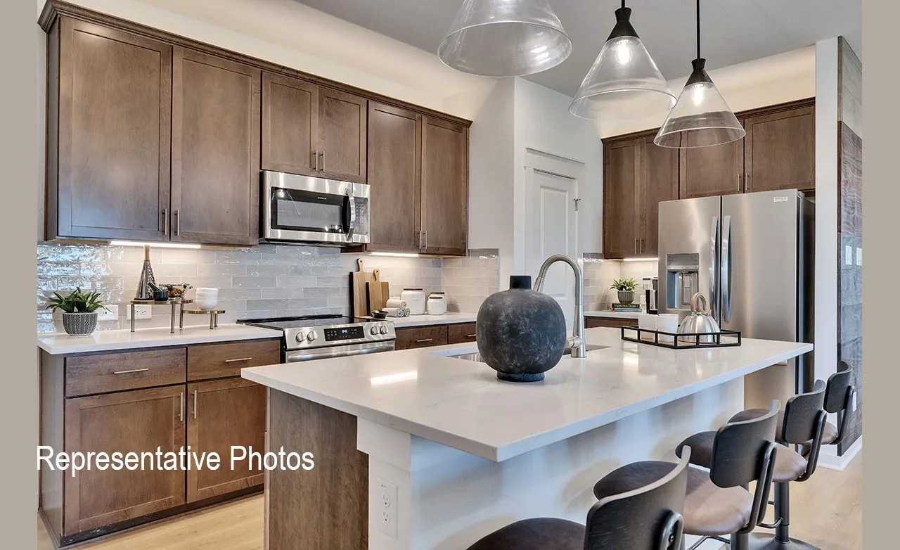 Modern kitchen featuring rich wood-finish cabinetry, stainless steel appliances, a light-toned countertop, a tile backsplash, and an island with pendant lighting
