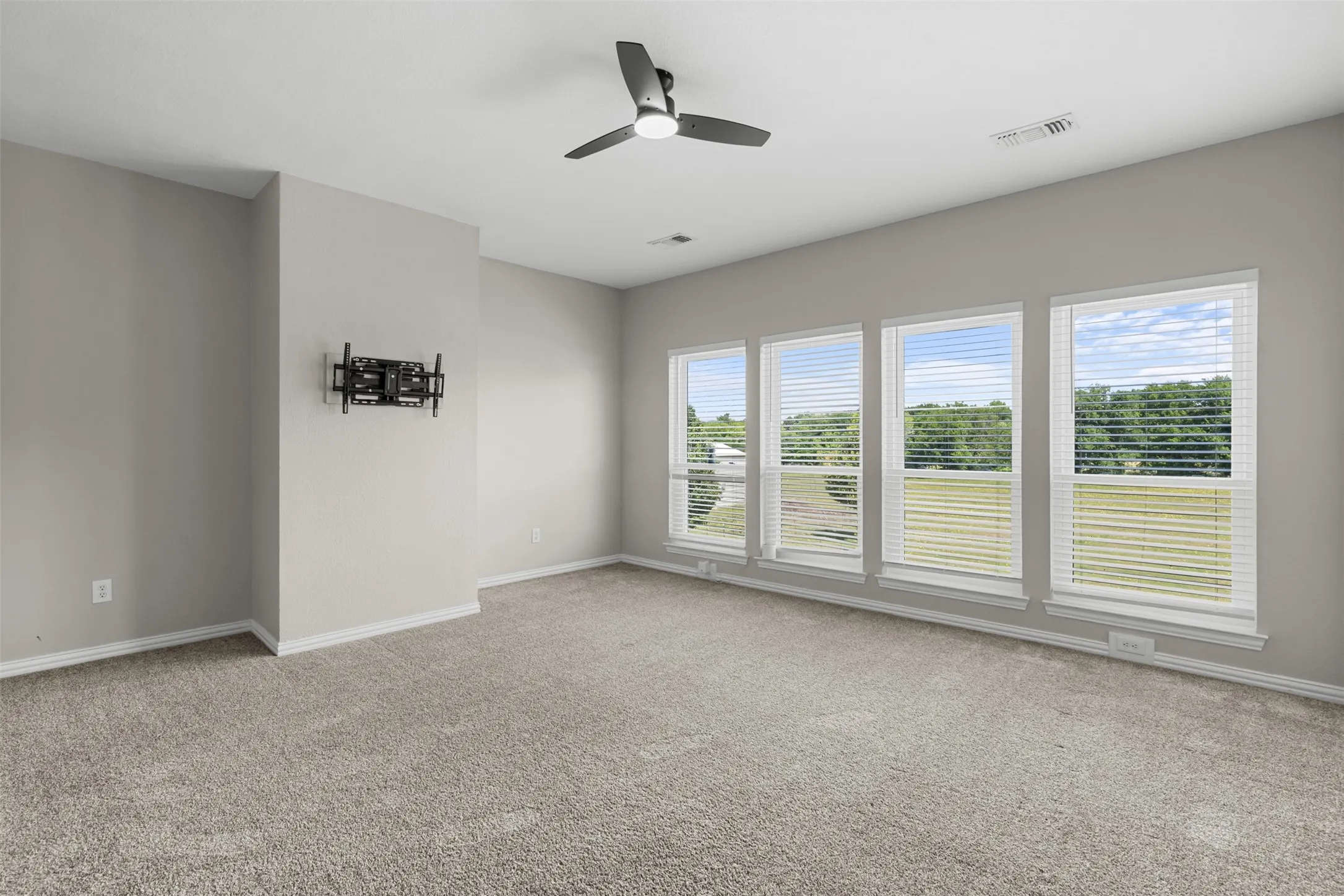 Spacious room featuring four large windows with blinds, light gray carpet, and a ceiling fan with integrated lighting
