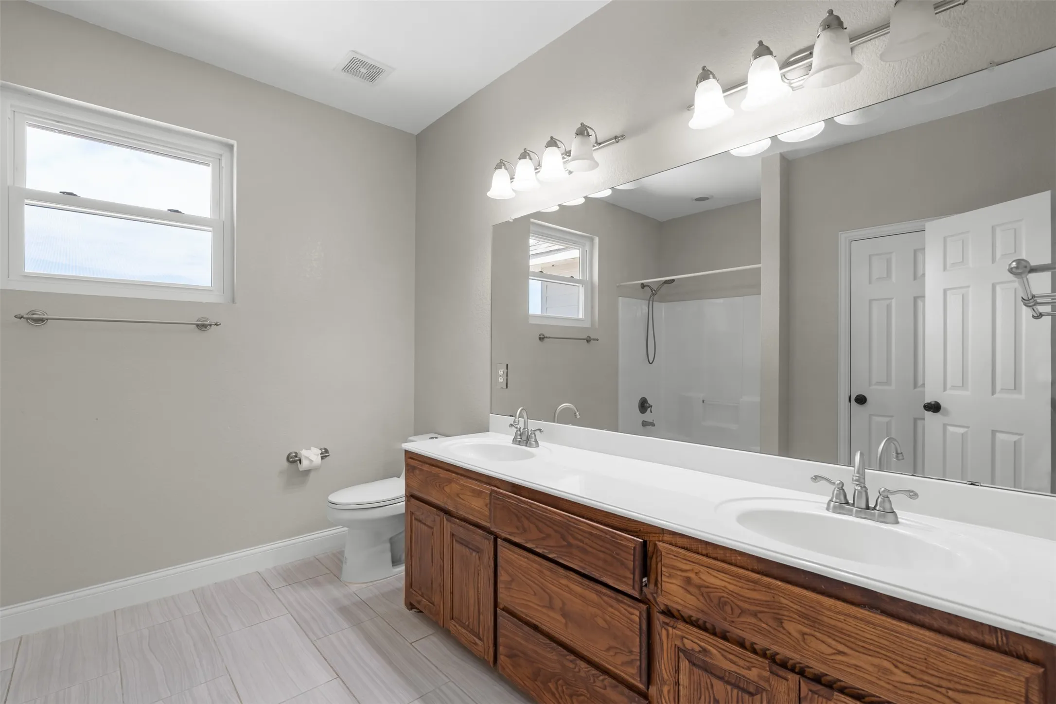Bathroom upstairs featuring a double vanity with wood cabinetry, white countertops, dual undermount sinks with chrome faucets, and an expansive wall mirror
