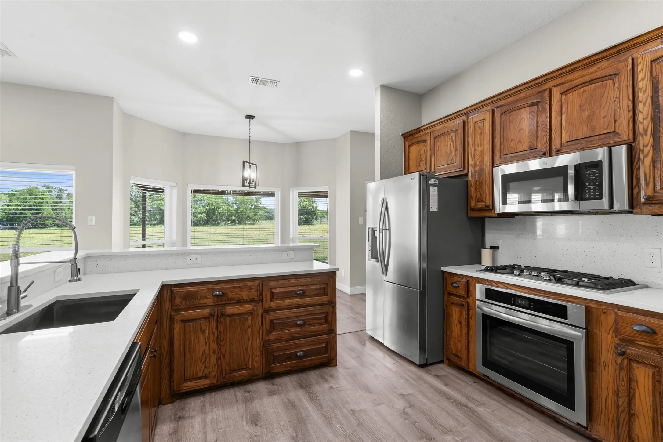 Kitchen featuring wood-finish cabinetry, light-toned countertops, and stainless steel appliances including a refrigerator, microwave, and oven with a gas cooktop