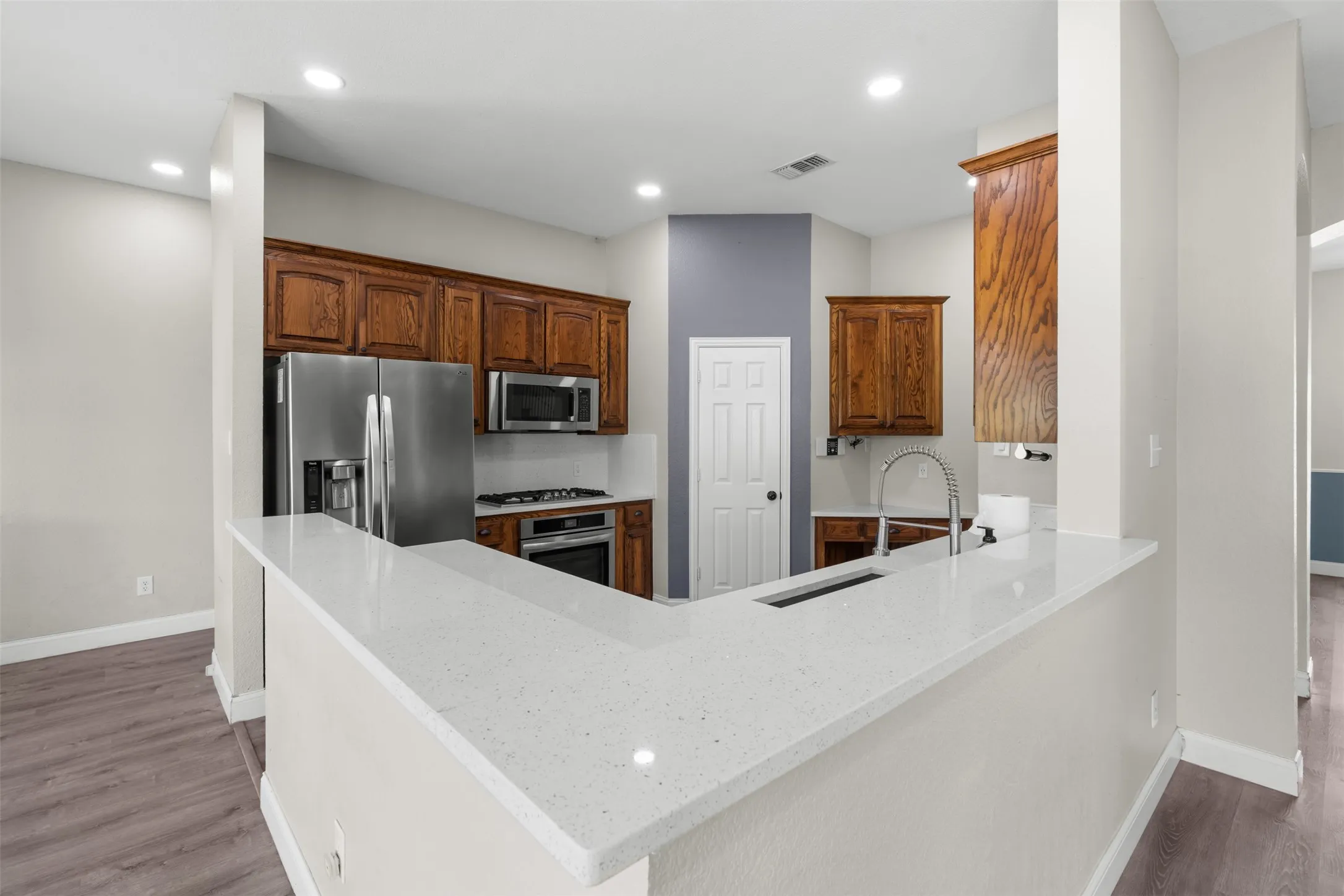 Kitchen featuring a large L-shaped countertop, wood-finish cabinetry, stainless steel appliances, and wood-finish flooring