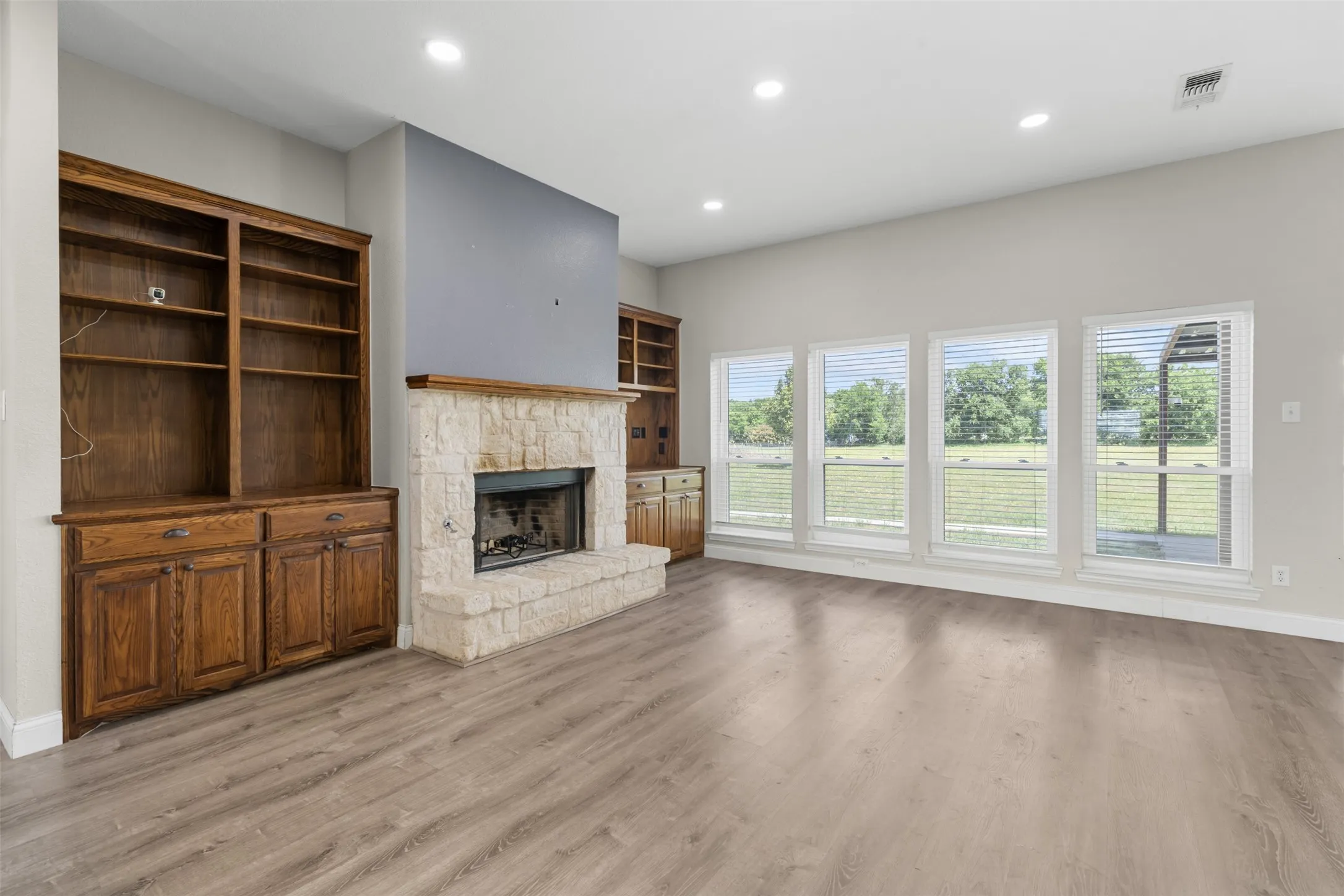 Spacious living area featuring light wood-finish flooring, a stone-clad fireplace, and built-in wood cabinetry