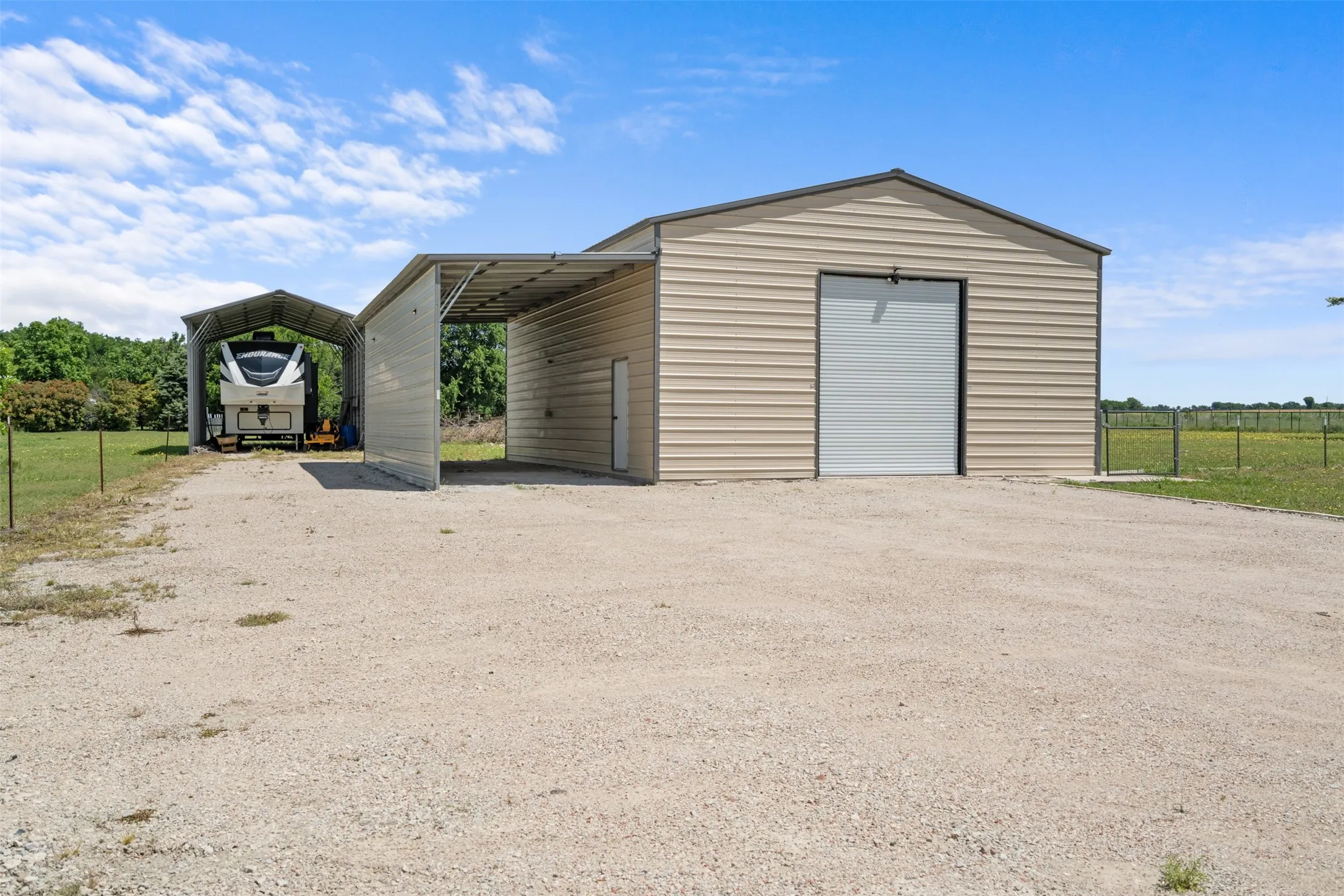 Beige metal workshop with a roll-up door and side entry door, featuring an attached carport