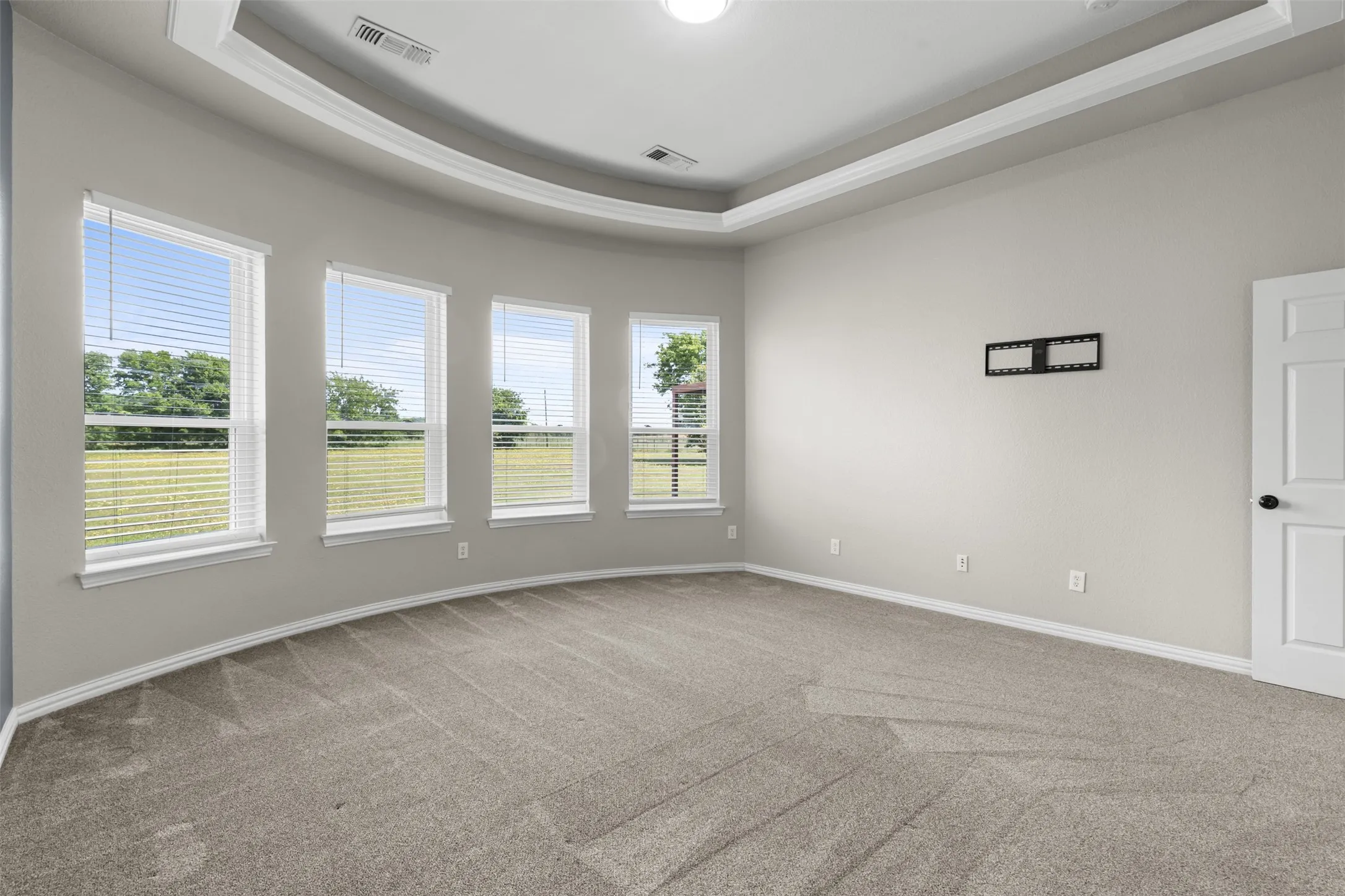 Spacious room featuring a curved wall with multiple windows, tray ceiling, neutral carpet flooring, and a white paneled door