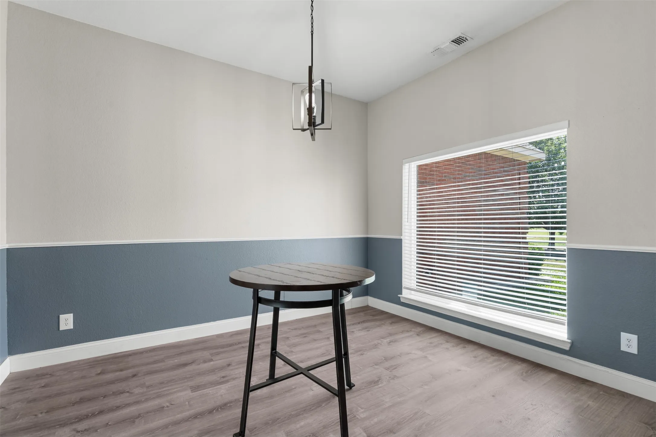 Interior space featuring two-tone walls, wood-finish flooring, a contemporary ceiling light fixture, and a large window with blinds
