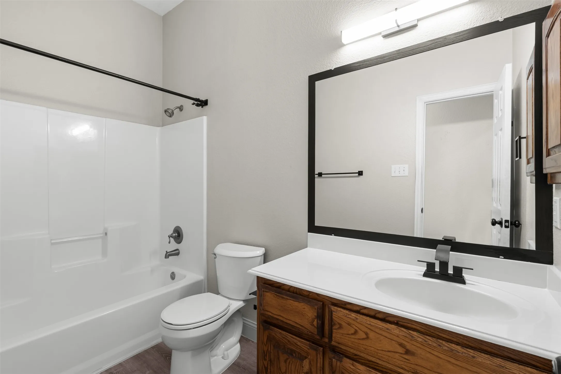 down stairs Bathroom featuring a white tub-shower combination, wood-finish vanity, integrated sink with matte black faucet, and a large framed mirror