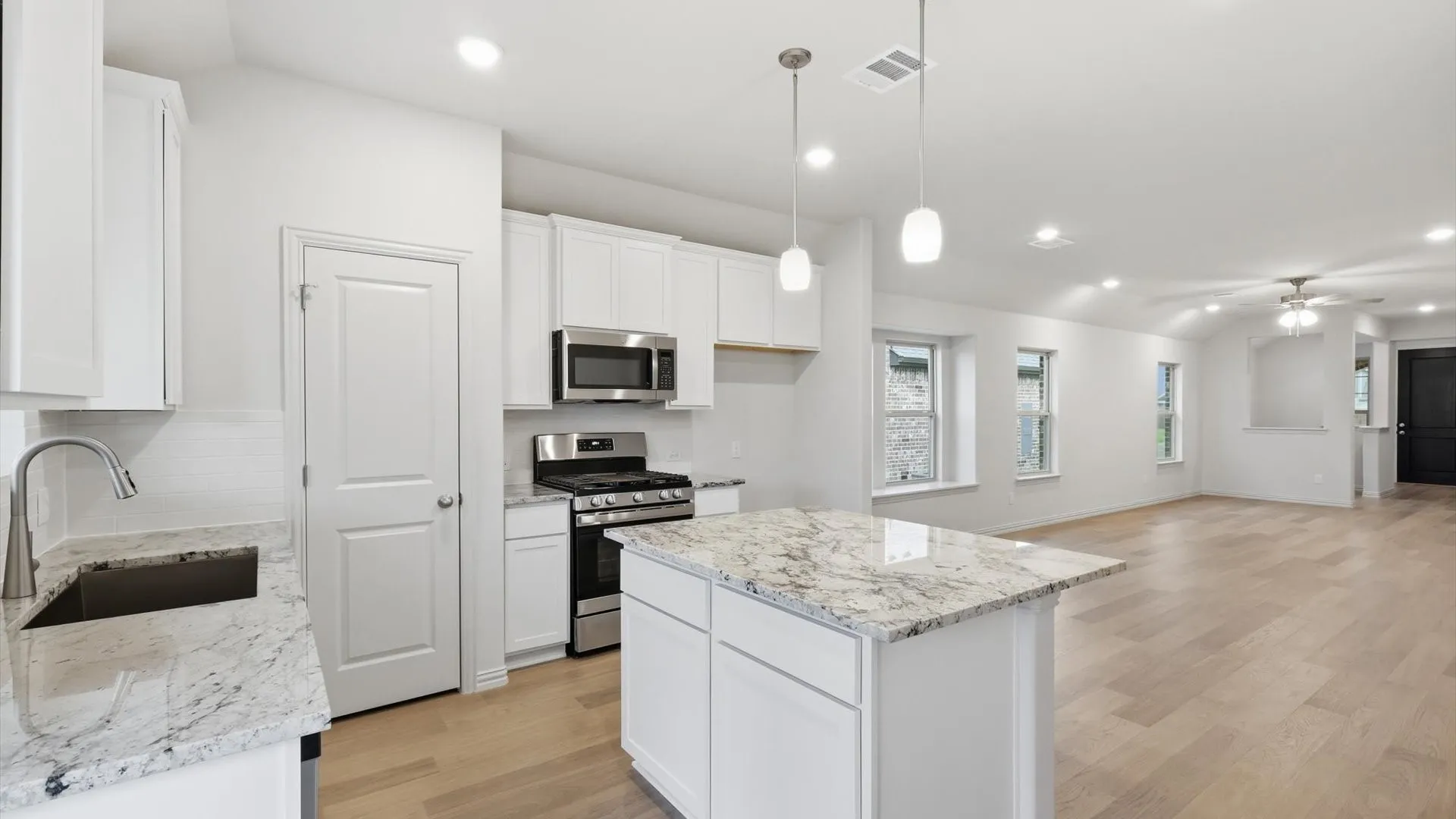 Open-concept kitchen and living area featuring white cabinetry, light-toned wood-finish flooring, a kitchen island with pendant lighting, stainless steel appliances, and recessed lighting throughout