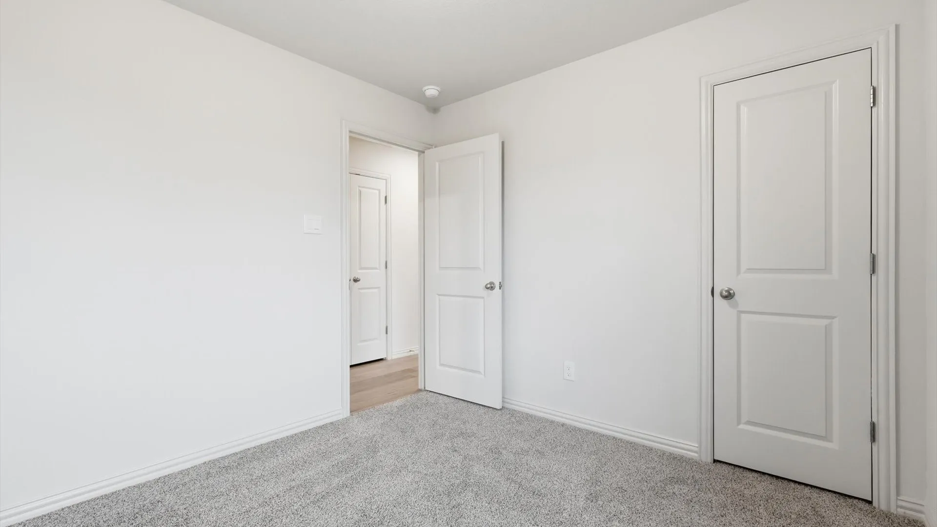 Neutral-toned interior featuring grey carpeting, white painted walls, white baseboards, and white two-panel interior doors with chrome hardware