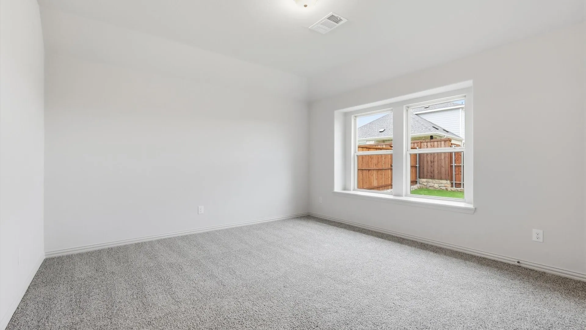 Carpeted room with a double window overlooking a fenced yard and light-colored walls