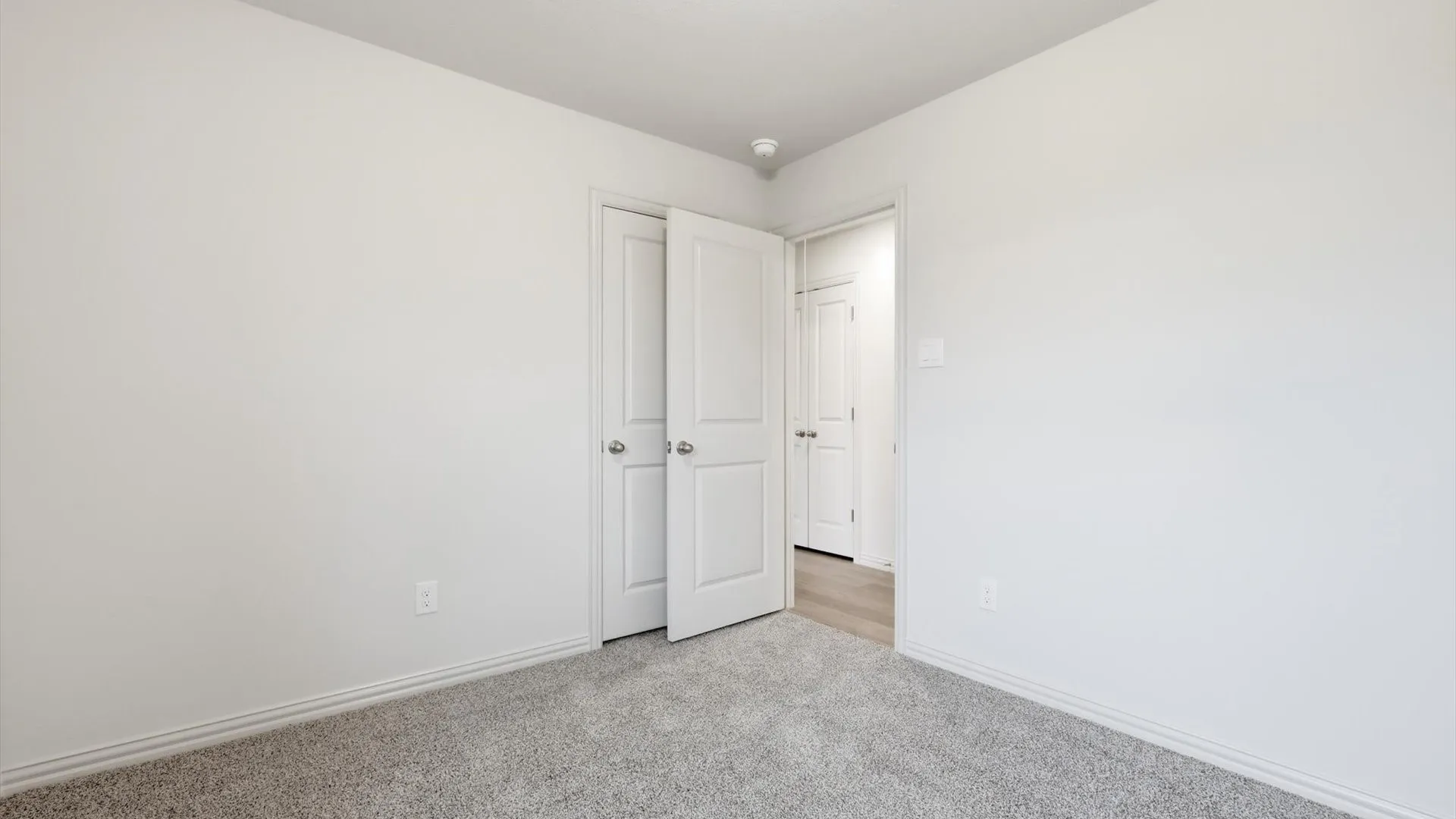 Neutral gray carpeted room with white painted walls, white trim, and white interior doors