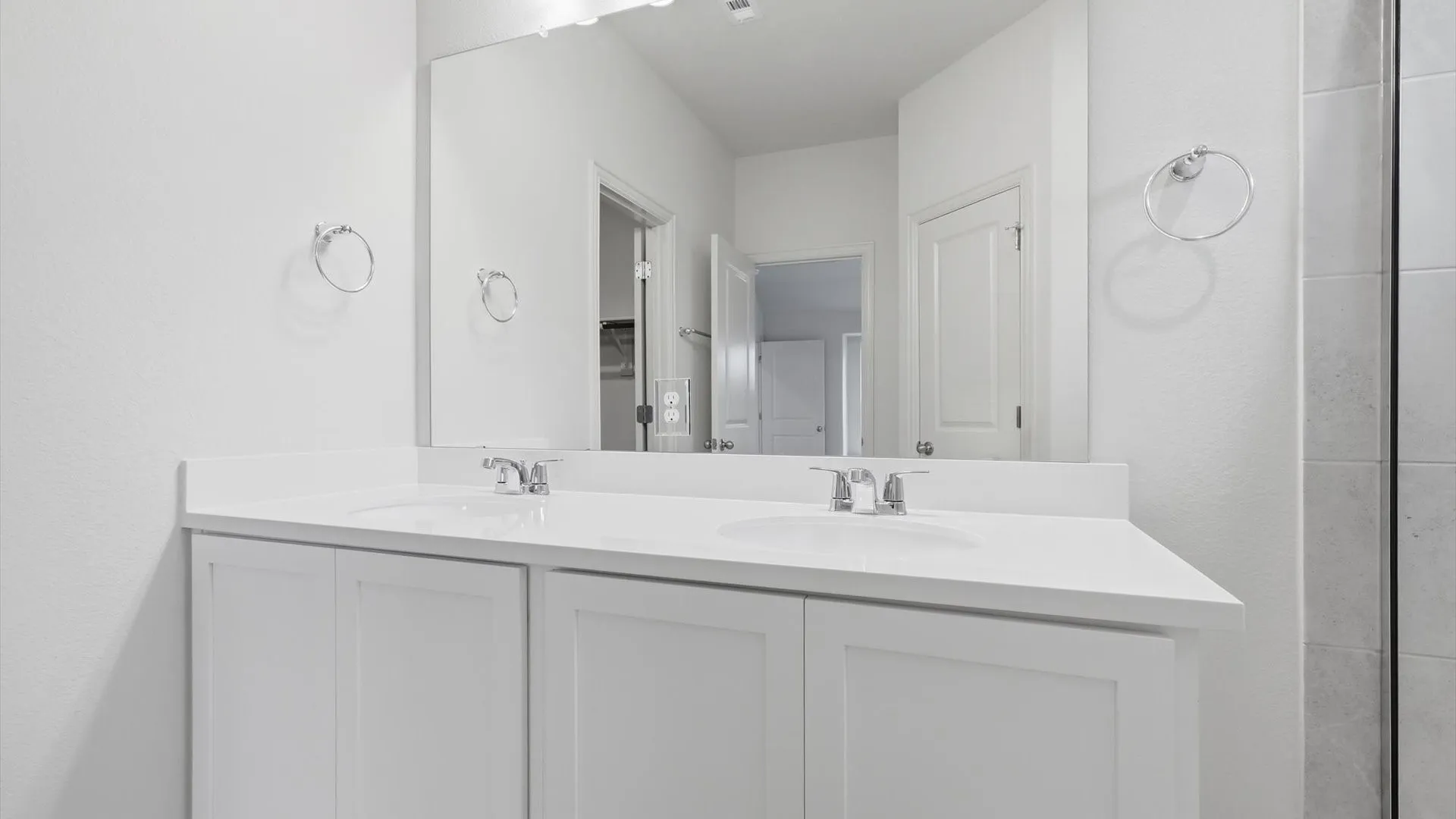 Dual vanity featuring white cabinetry, integrated sinks, chrome faucets, and a large wall-mounted mirror