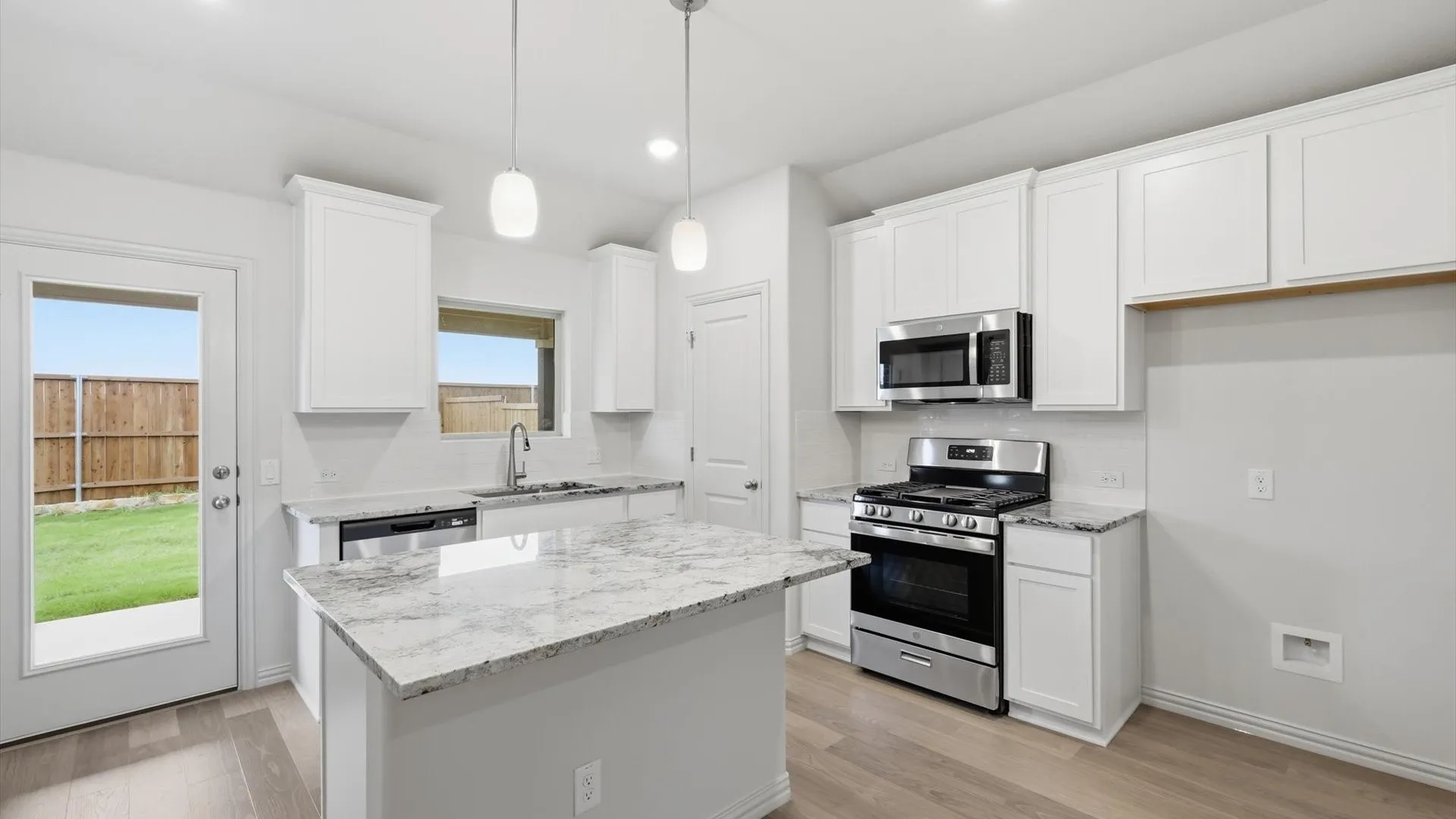 Contemporary kitchen featuring white cabinetry, light-toned wood-finish flooring, a central island with a stone-finish countertop, stainless steel appliances, and pendant lighting