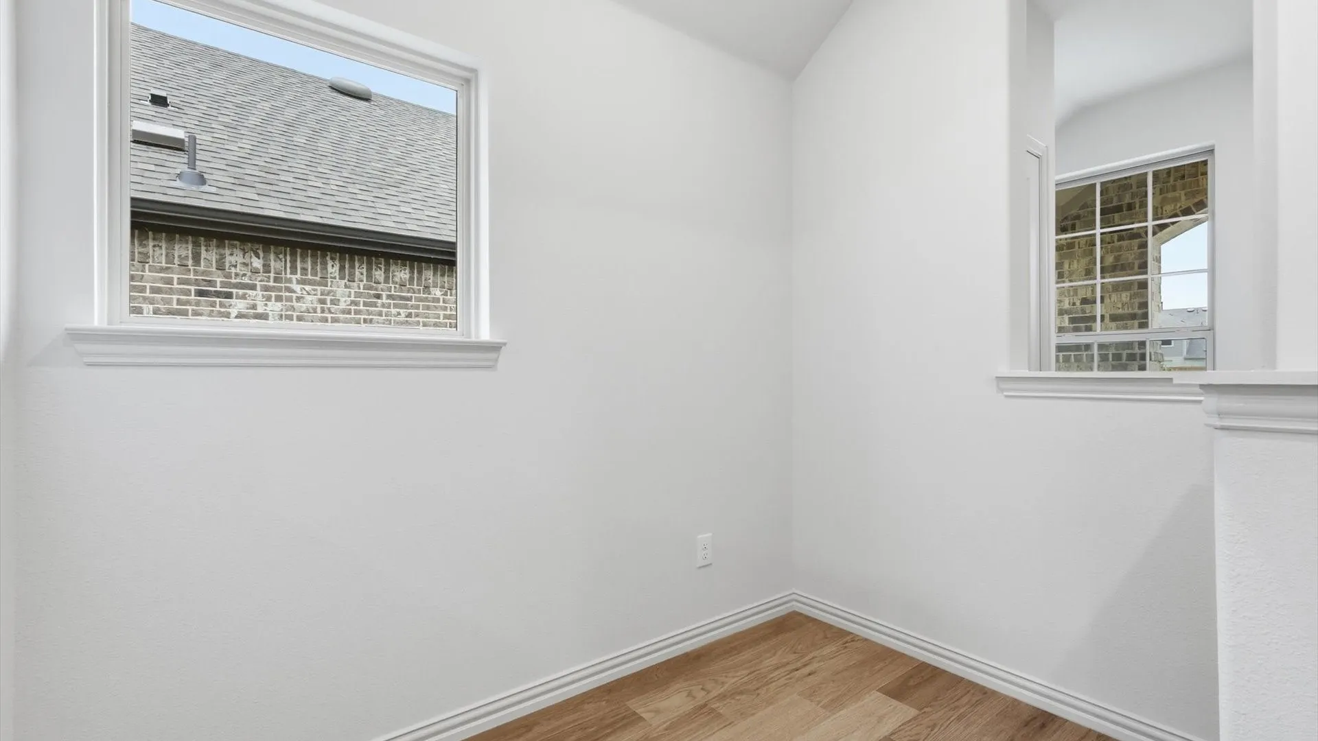 Recessed corner space featuring wood-finish flooring, crisp white walls, and a large window with white trim