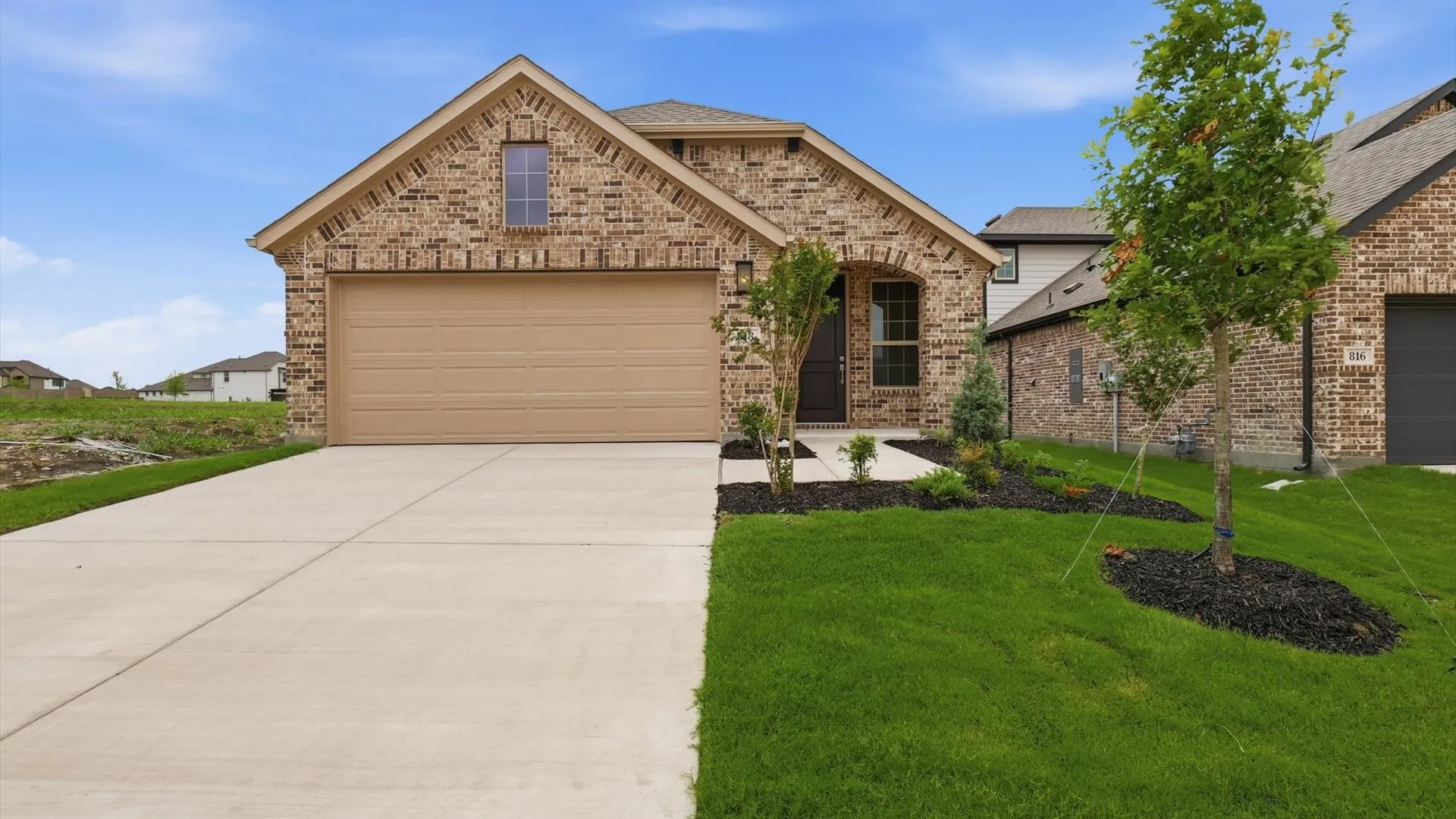 Brick facade residence featuring an attached garage, concrete driveway, and a manicured lawn