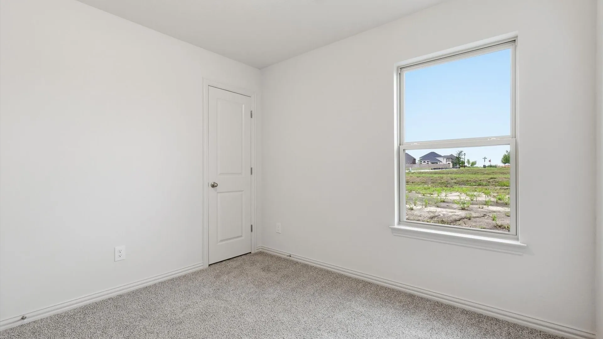 Bright room featuring a single-paneled interior door, white baseboards, light gray carpet, and a large window with white trim
