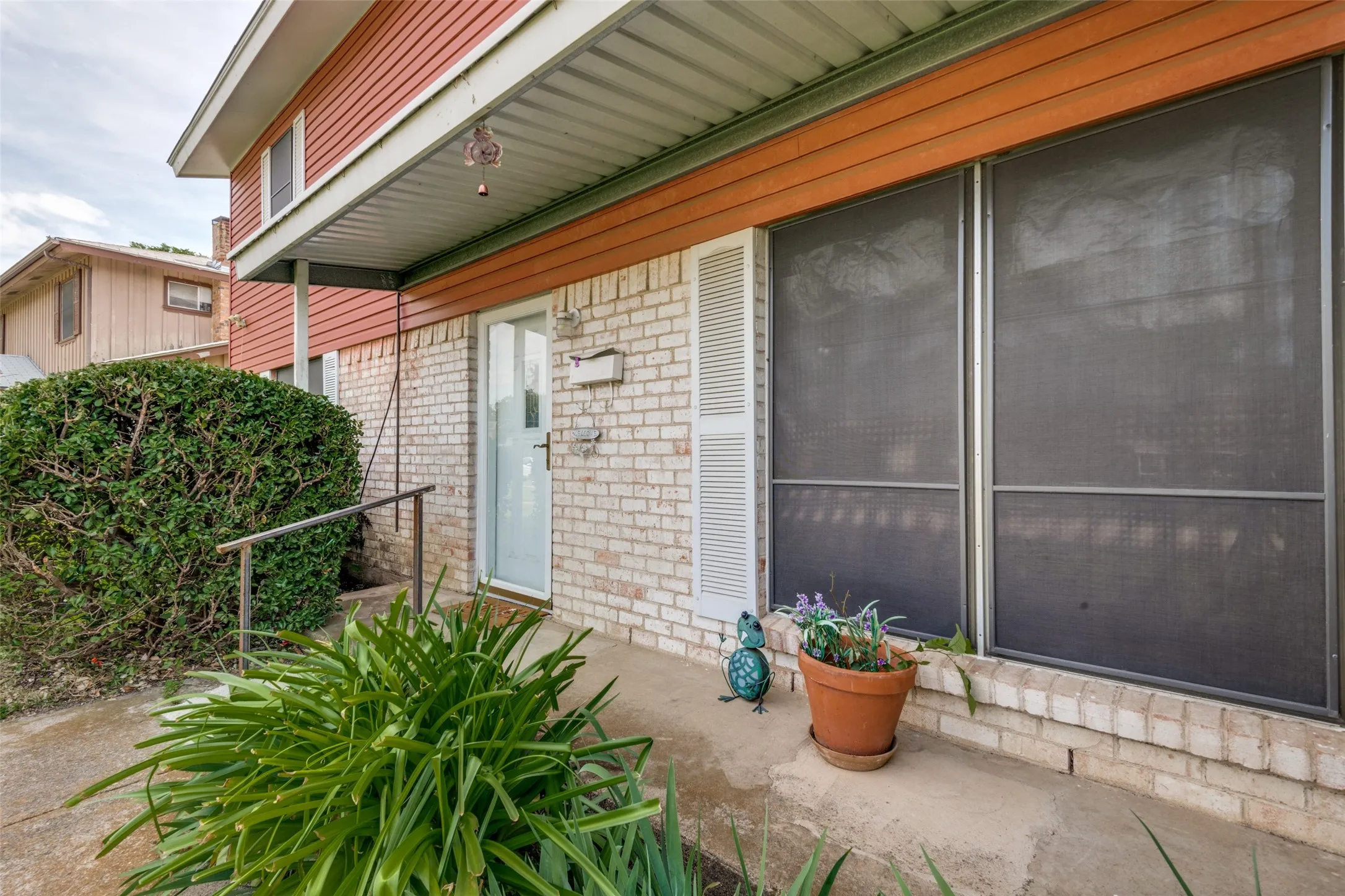 White brick exterior with a covered entryway, featuring an opaque glass entry door and a metal handrail