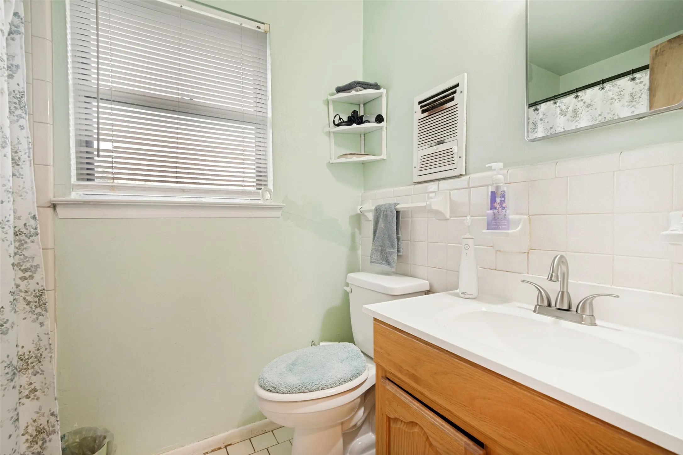 Bathroom featuring a wood-finish vanity with an integrated sink and chrome faucet, white tiled wainscoting, and a window with blinds