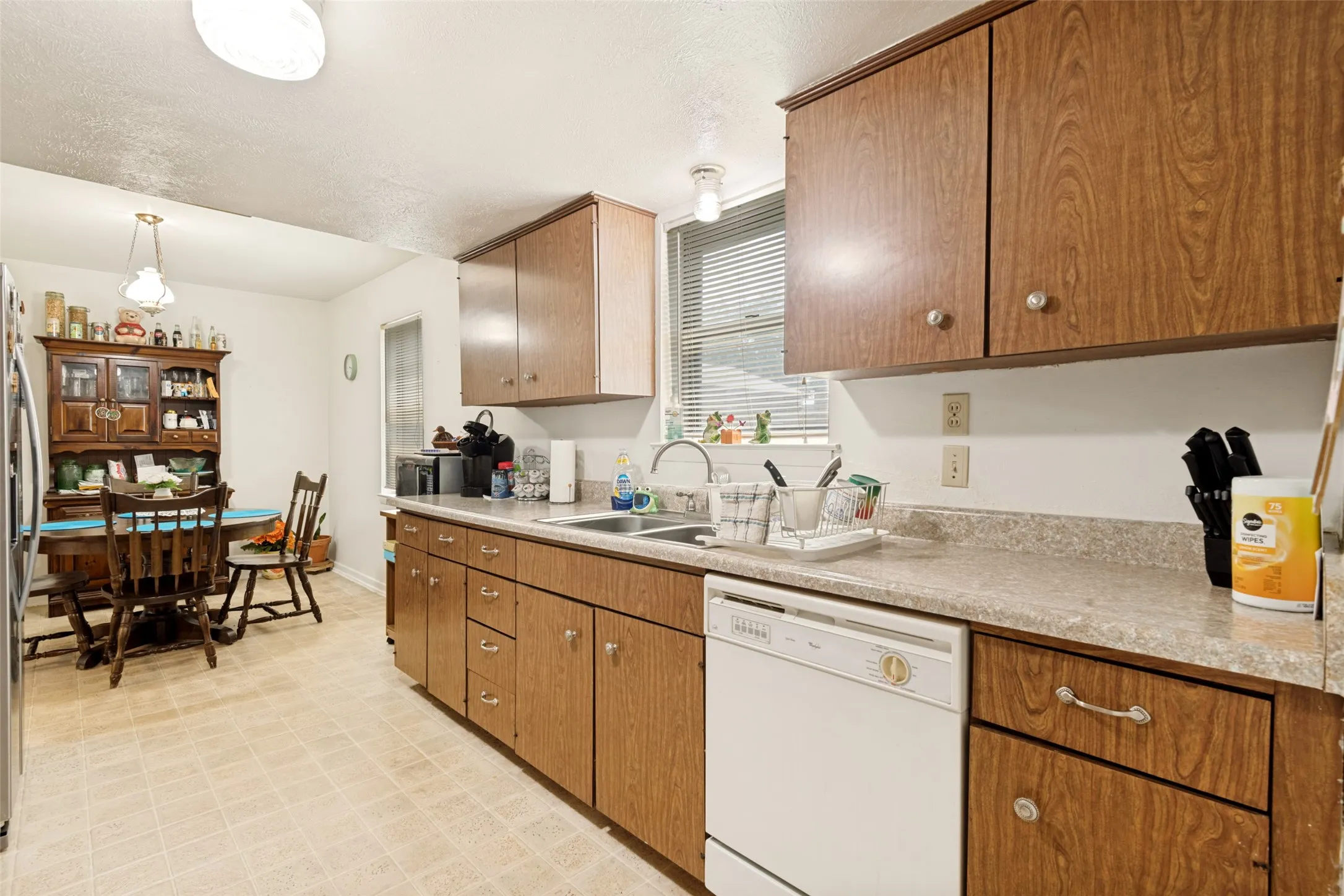 Kitchen featuring wood-finish cabinetry with silver-tone hardware, a double basin sink, and a white dishwasher