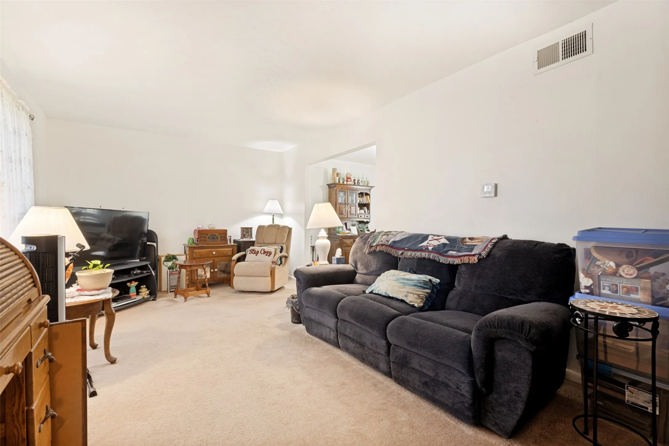 Carpeted living area featuring light-toned walls and an overhead air vent