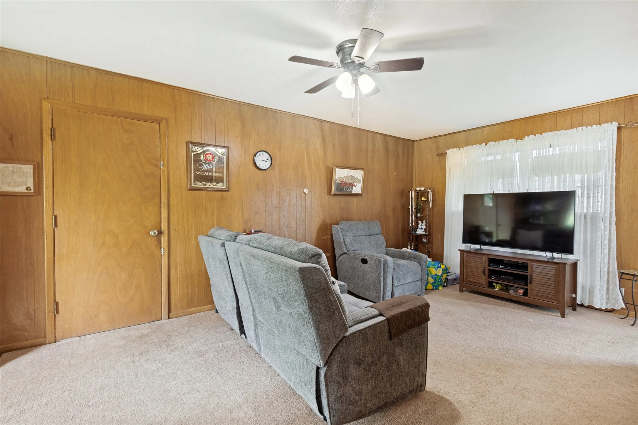 Living space featuring wood paneling, light-colored carpeting, a white ceiling, and a ceiling fan with integrated lighting