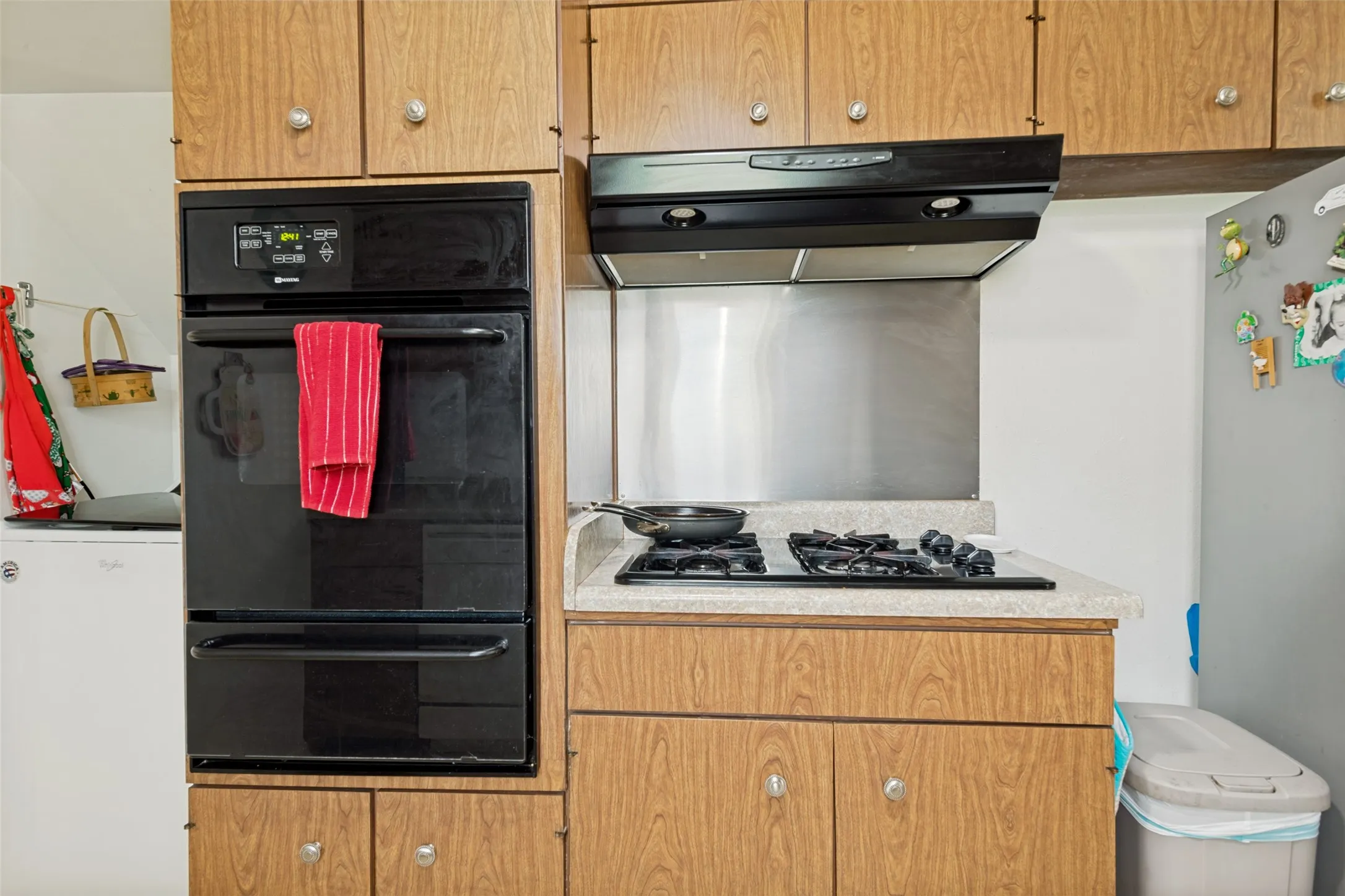 Kitchen featuring wood-finish cabinetry, a built-in wall oven, and a gas cooktop with an overhead range hood