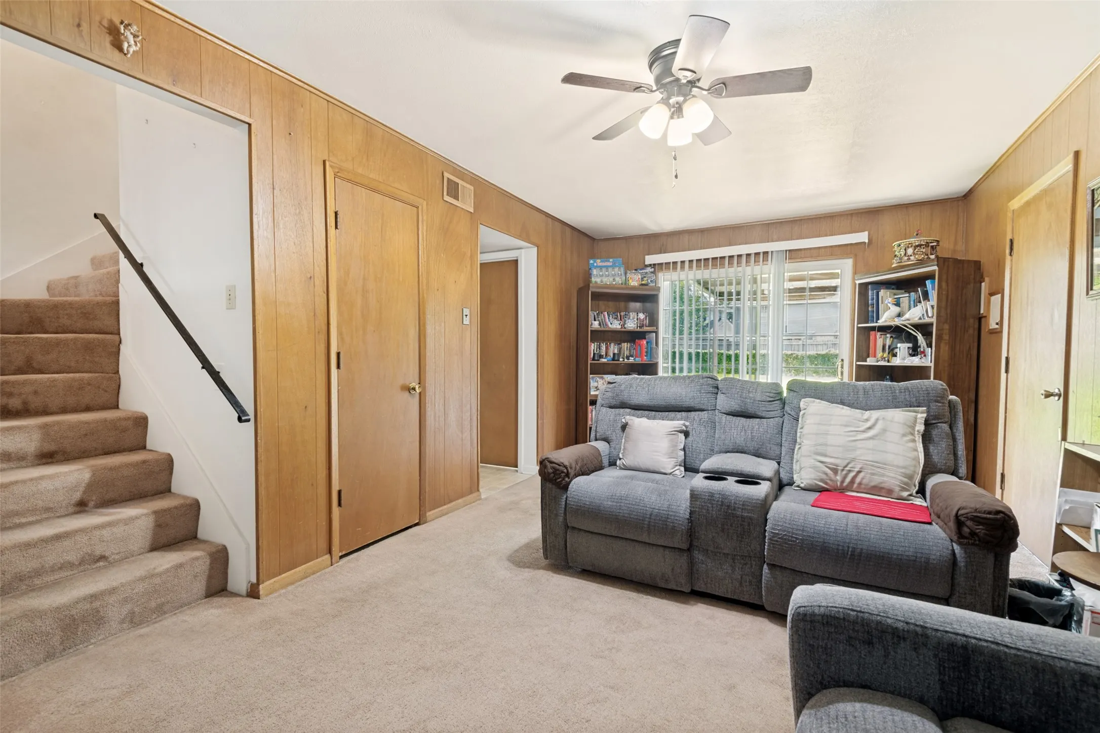 Living area featuring wood-finish wall paneling, carpeted flooring, and a ceiling fan