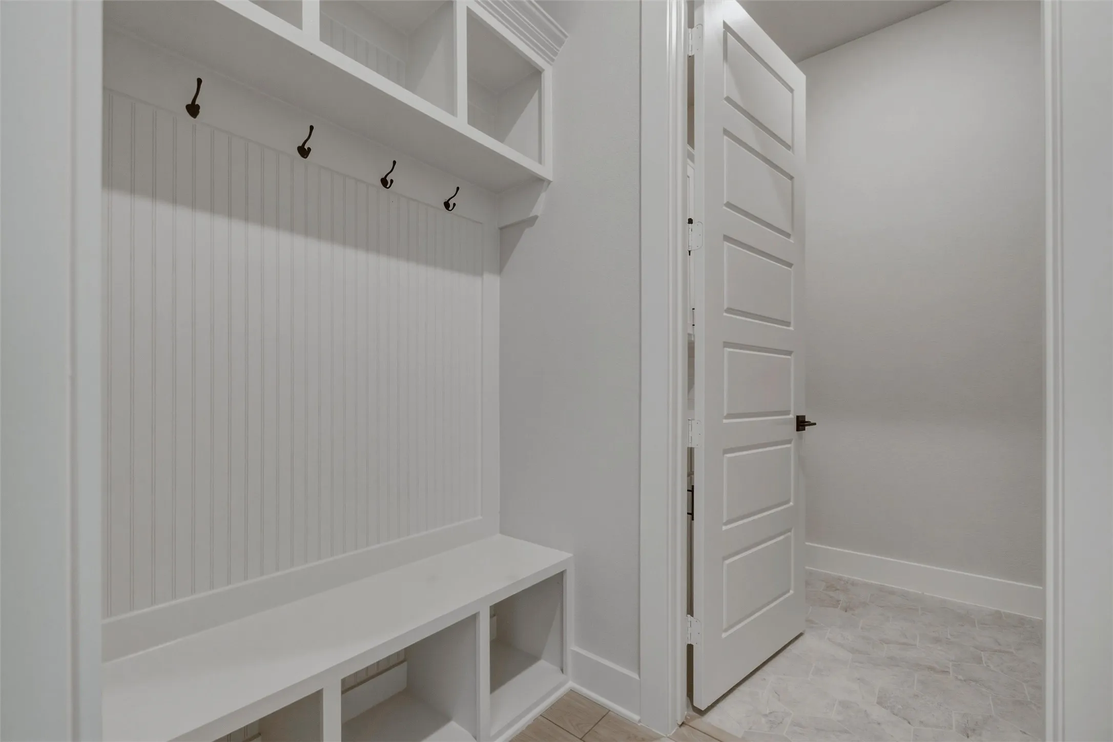 Built-in mudroom bench with cubby storage, beadboard paneling, and upper shelving