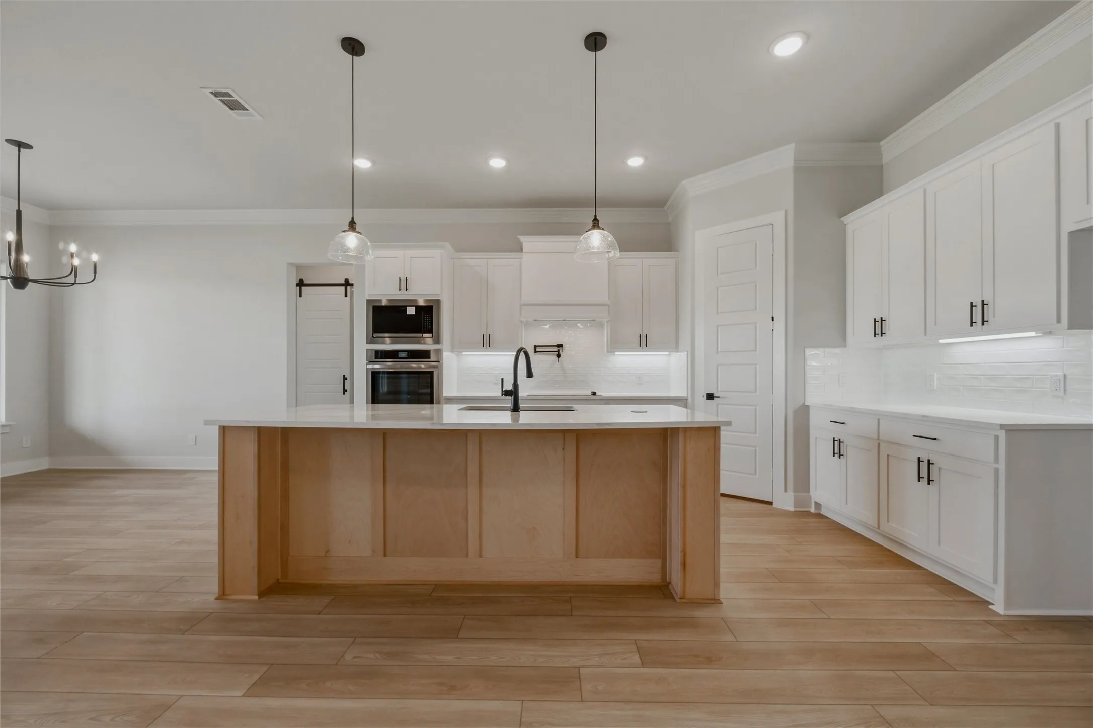 Spacious kitchen featuring an expansive center island, white cabinetry, built-in double ovens, and wood-finish flooring