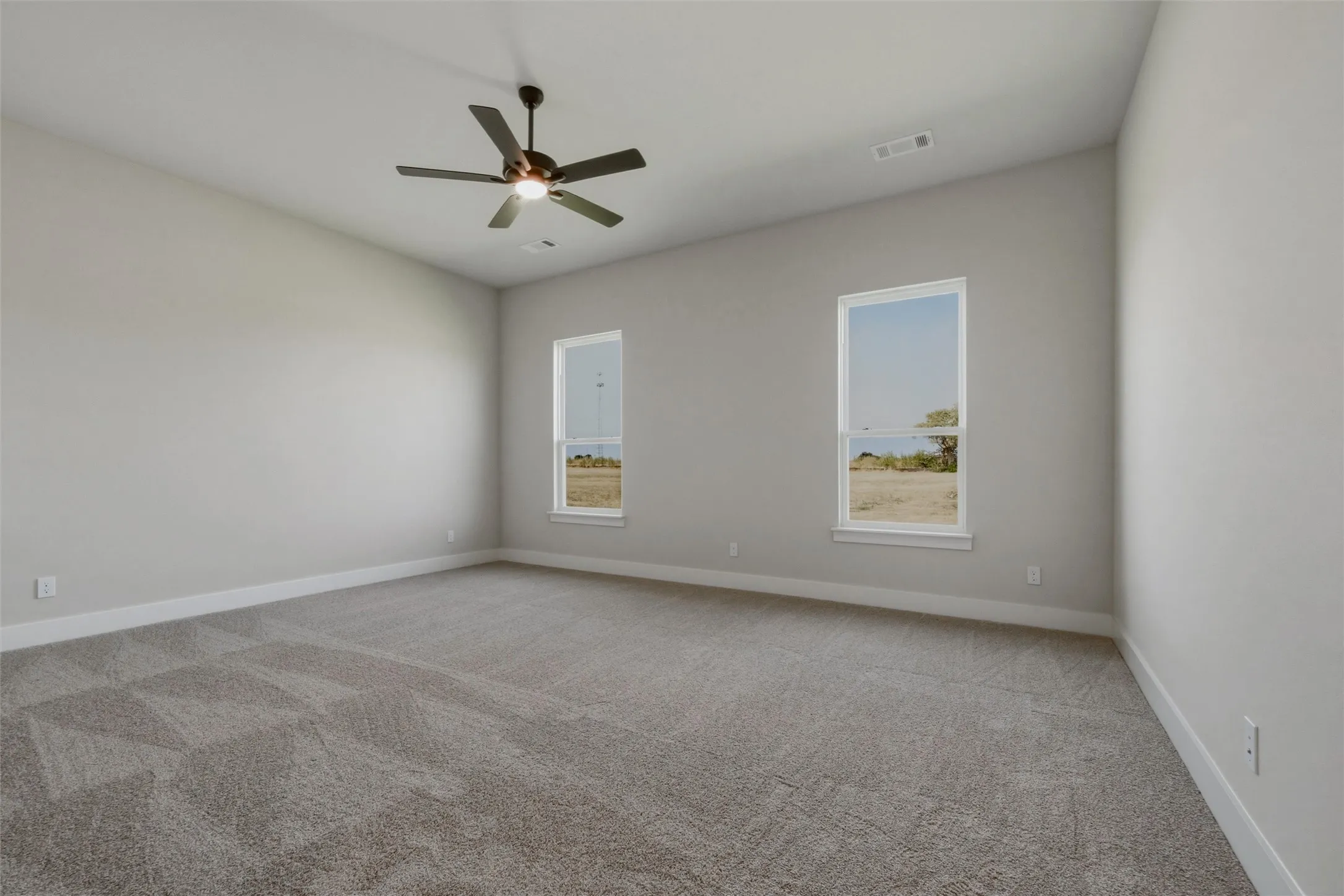 Spacious room featuring neutral carpeting, a ceiling fan with integrated lighting, two windows, and a vaulted ceiling
