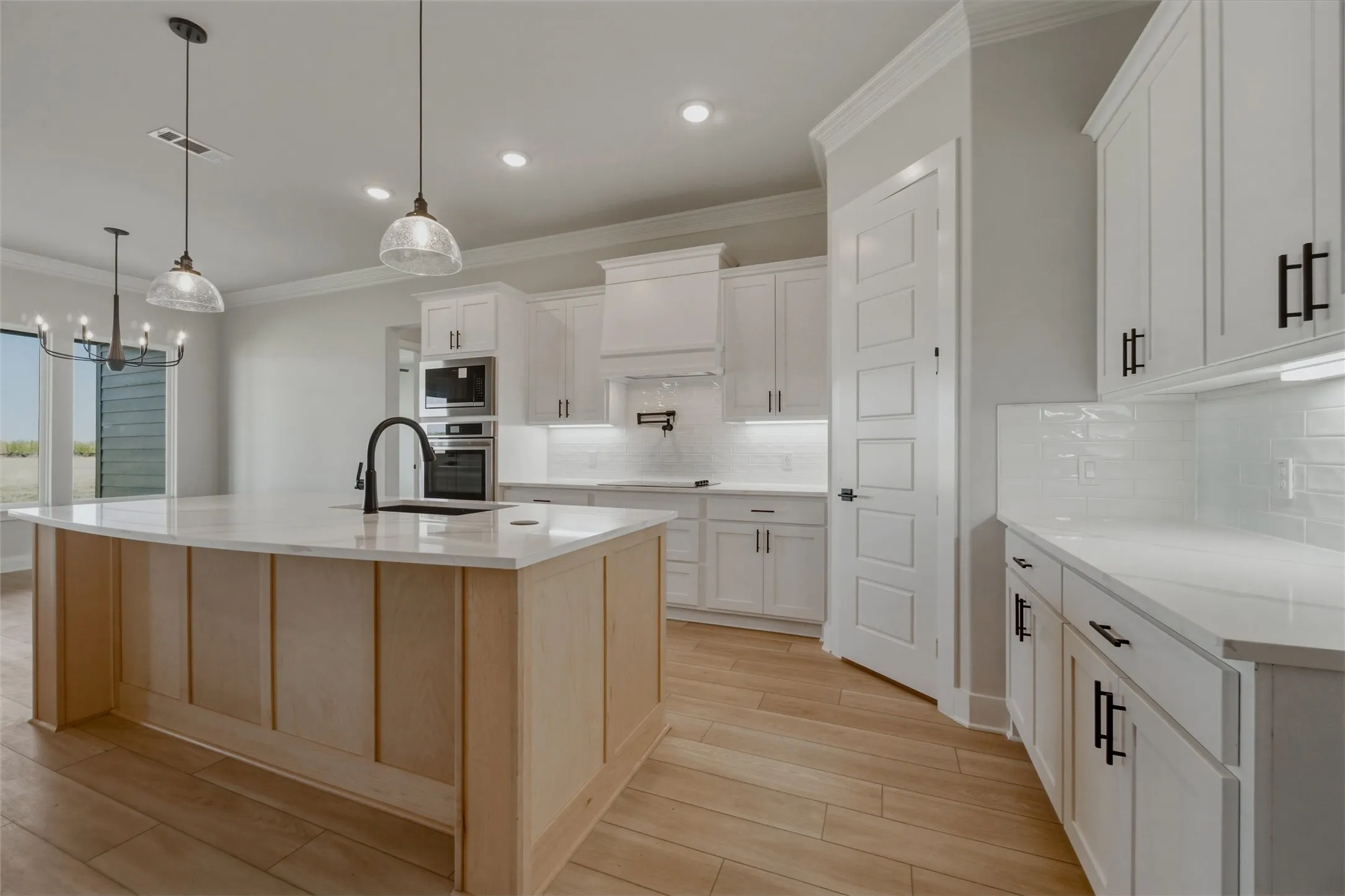 Kitchen featuring a light wood-finish island, white cabinetry with black hardware, white countertops, a white subway tile backsplash, and stainless steel built-in appliances
