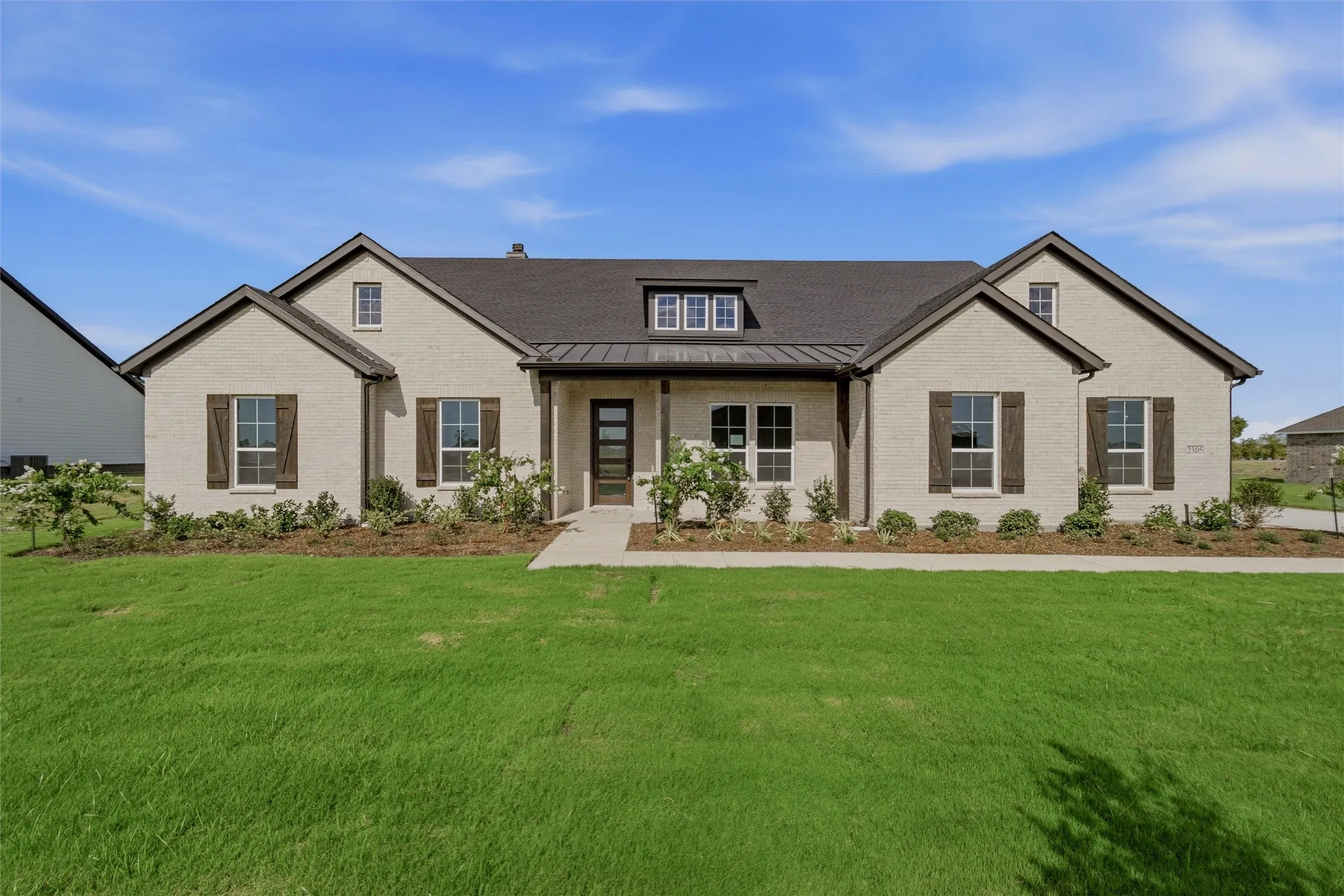 Brick exterior with a dark shingle roof, dark wood shutters, and an inviting front entry