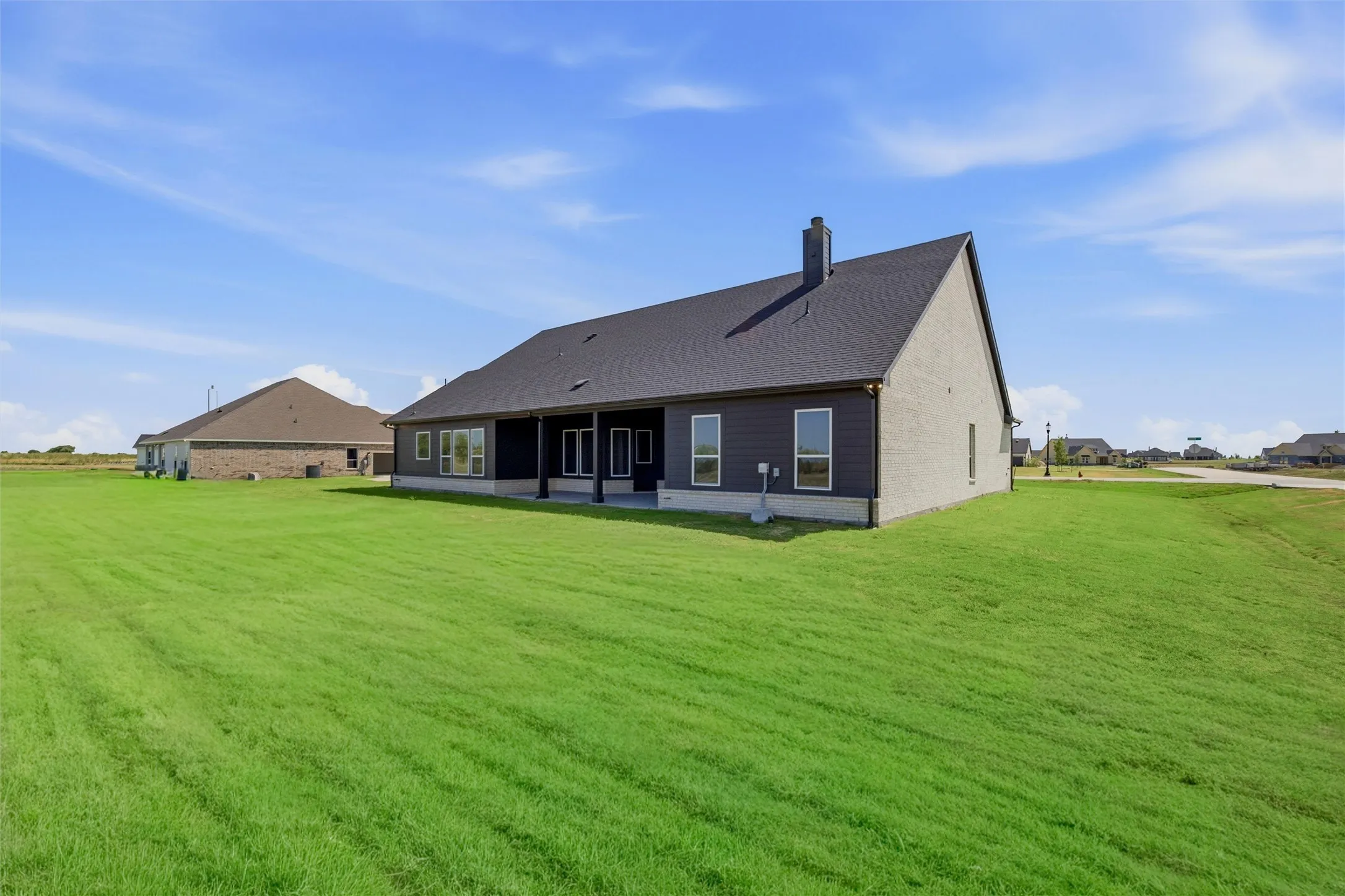 Expansive green lawn surrounding a residence with a dark shingle roof, light-colored siding, and a covered patio