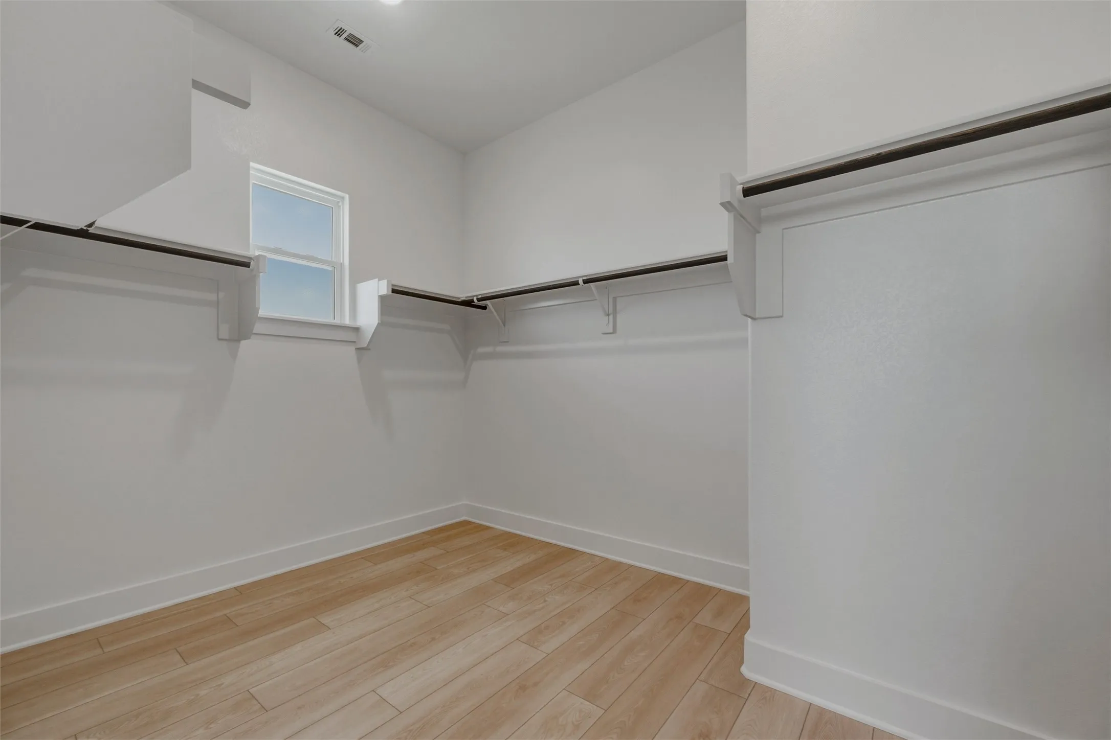 Expansive closet with wood-finish flooring, white walls, built-in shelving, and a prominent window