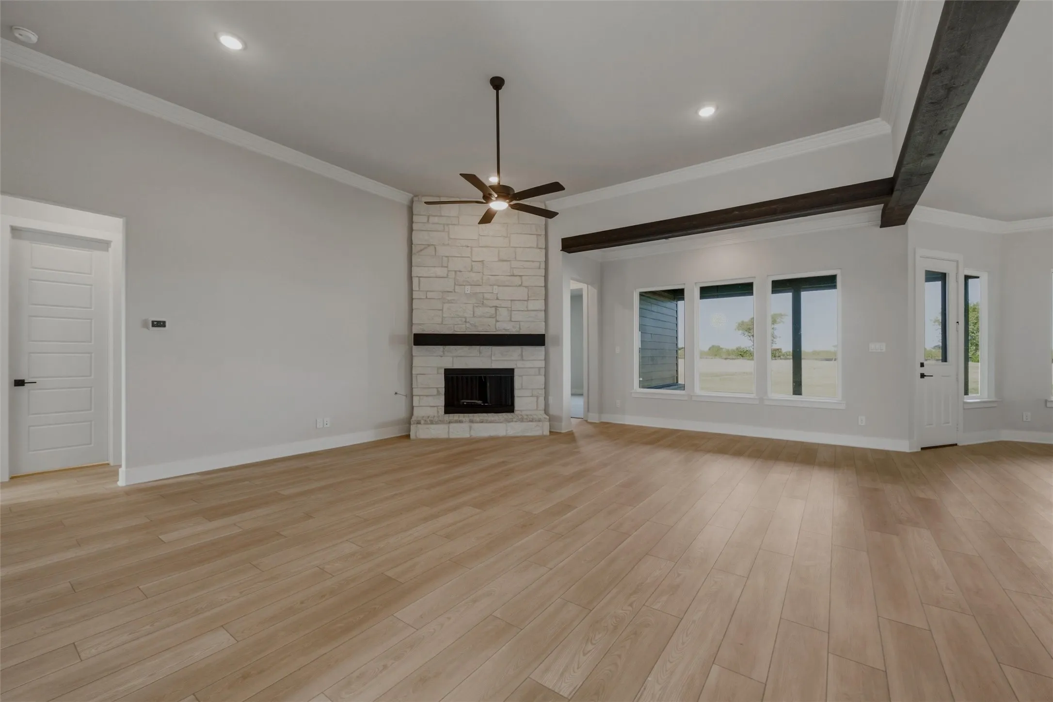 Expansive room featuring wood-finish flooring, a stone-clad fireplace with a dark wood mantle, and exposed dark wood ceiling beams