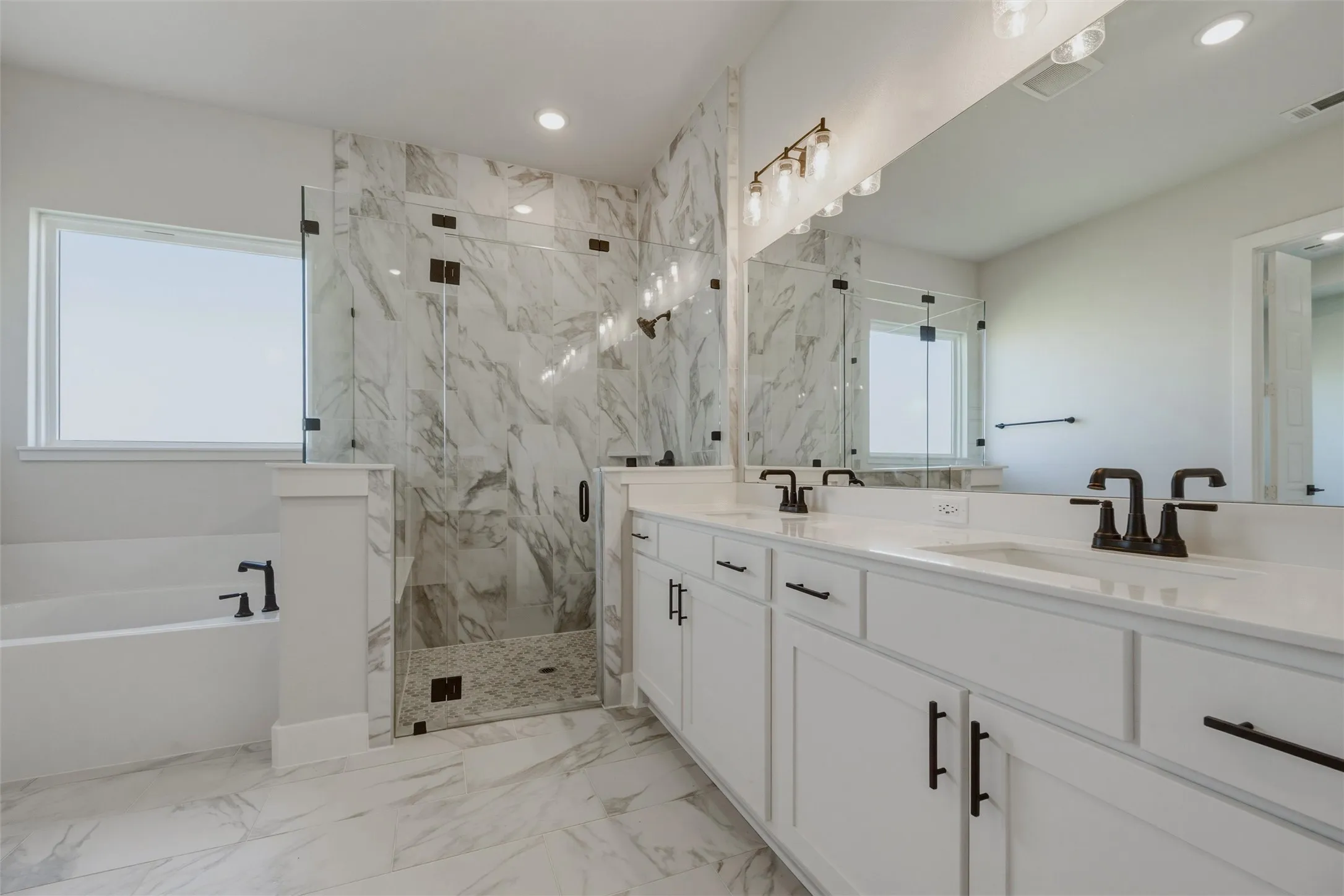 Dual vanity with white cabinetry and dark bronze hardware, walk-in shower with glass enclosure, separate soaking tub with dark bronze fixtures, marble-look tile flooring, and integrated lighting