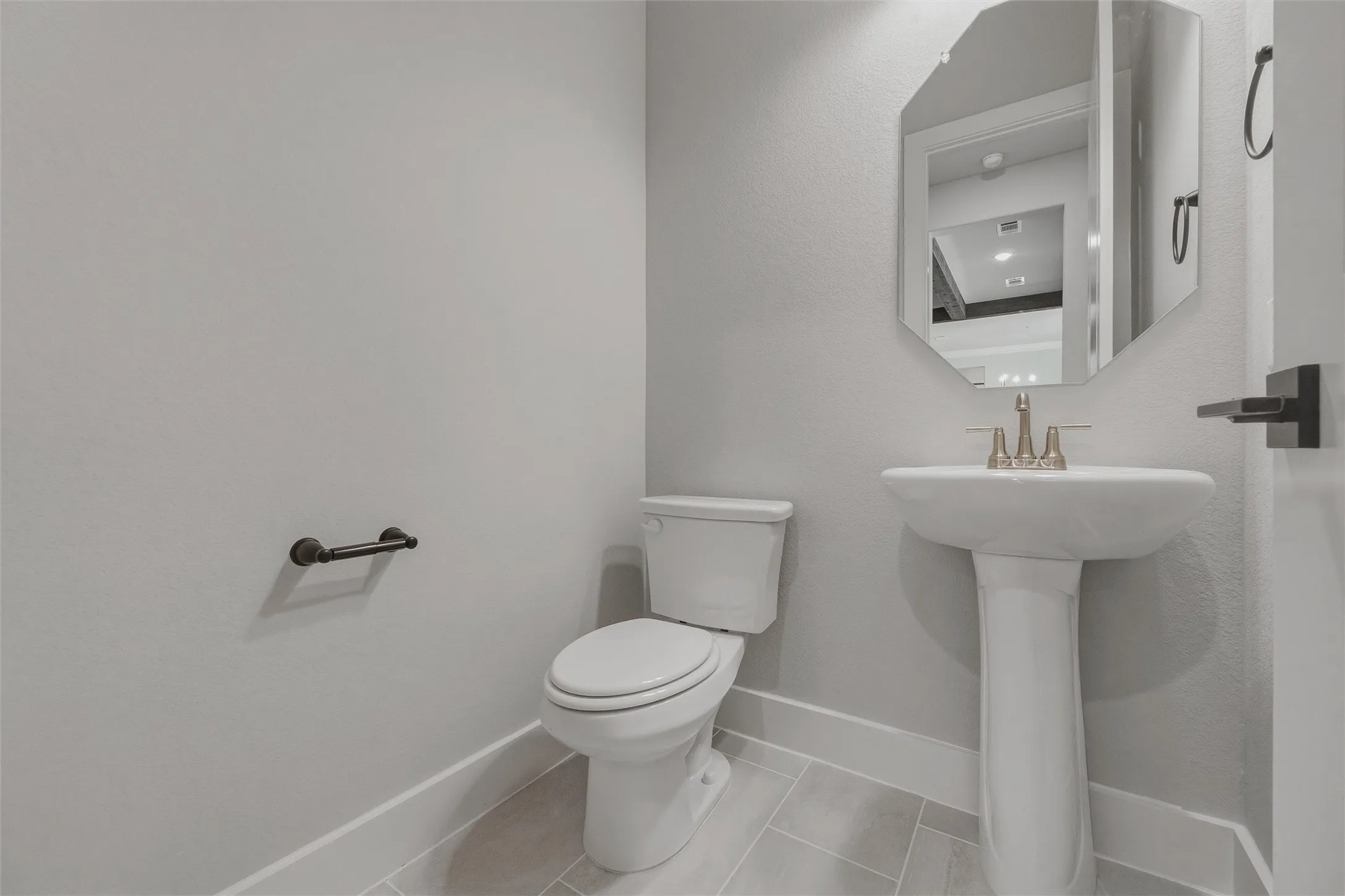 Pedestal sink with a decorative mirror, modern toilet, and light-toned tile flooring