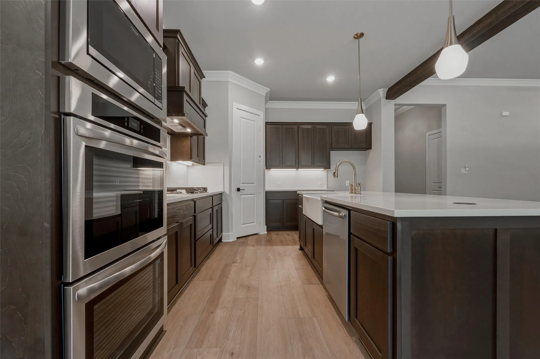 Stainless steel double wall ovens and microwave, dark wood-finish cabinetry, light wood-finish flooring, white countertop island, and pendant lighting