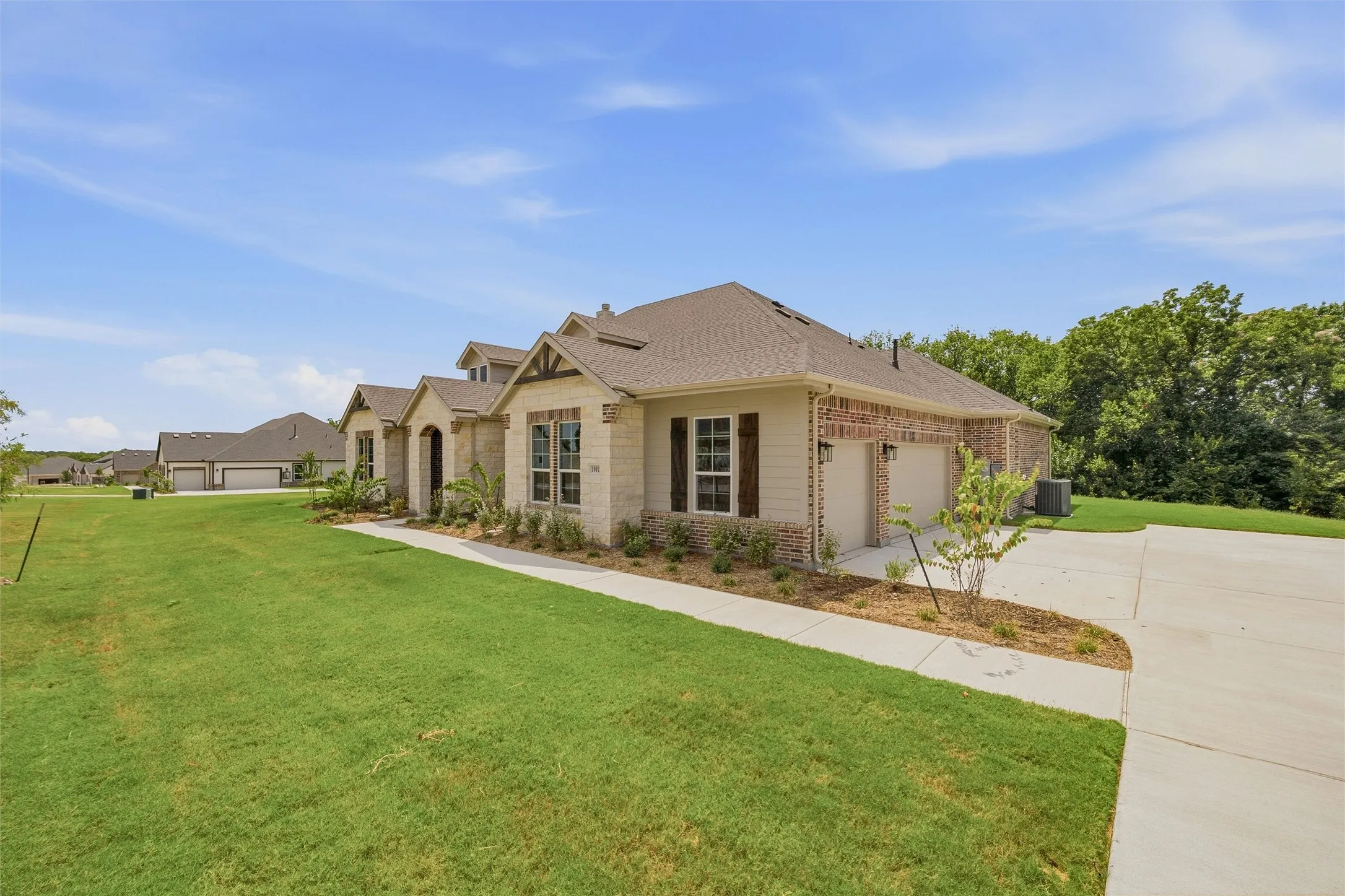 Craftsman-style exterior with stone and brick accents, attached two-car garage, concrete driveway, and front landscaping