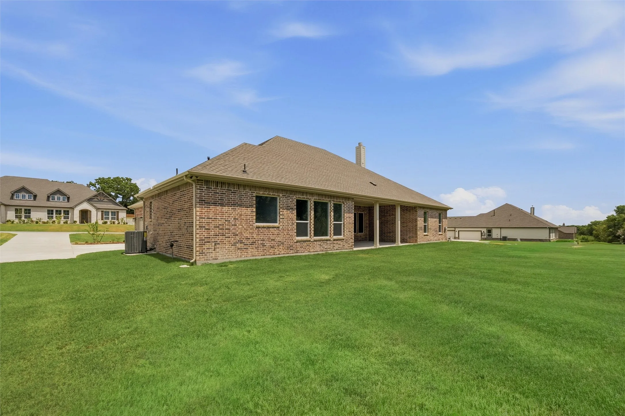 Brick exterior with a covered patio, multiple windows, and a large grassy yard