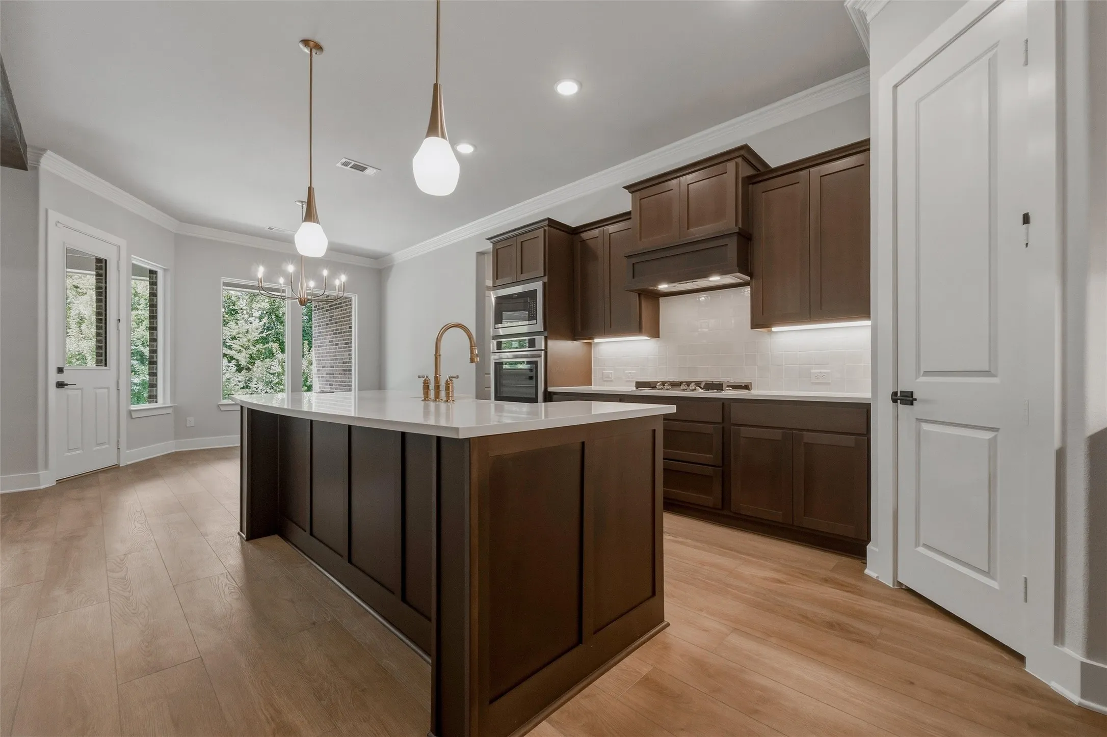 Kitchen featuring a central island with white countertop, dark wood-finish cabinetry, wood-finish flooring, integrated wall ovens, and pendant lighting