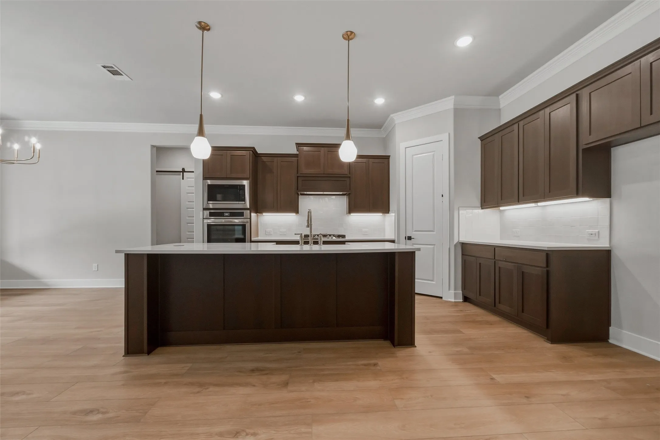 Kitchen featuring a central island, wood-finish flooring, dark wood cabinetry, built-in stainless steel appliances, and under-cabinet lighting