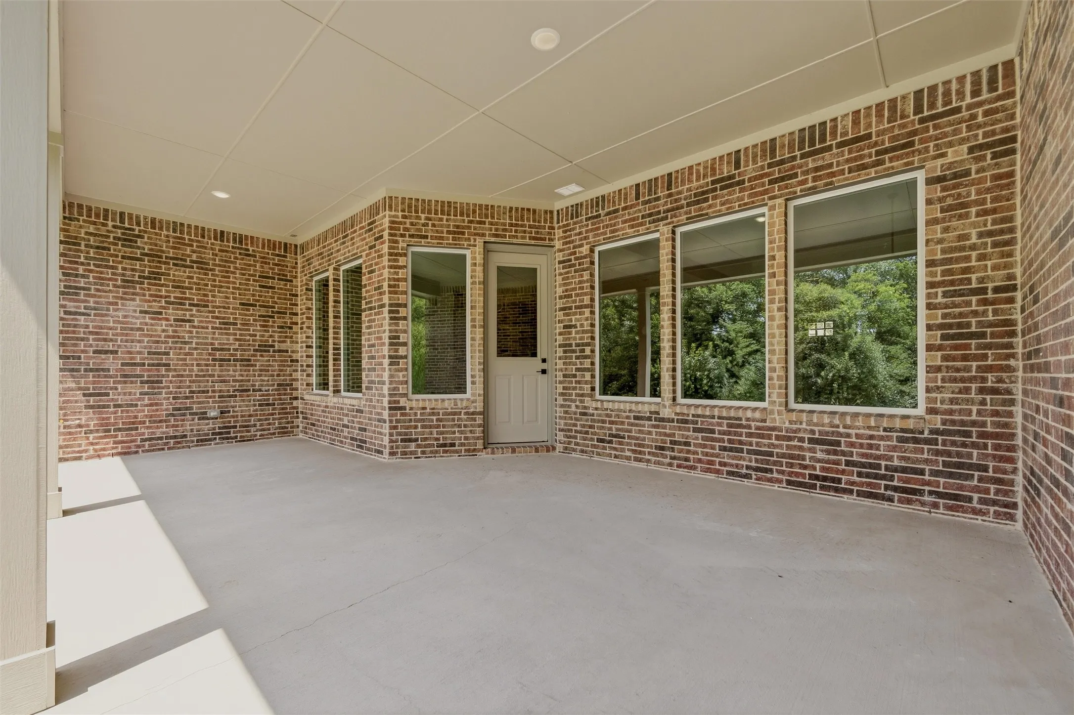 Expansive covered patio featuring a concrete surface, brick walls, and multiple windows