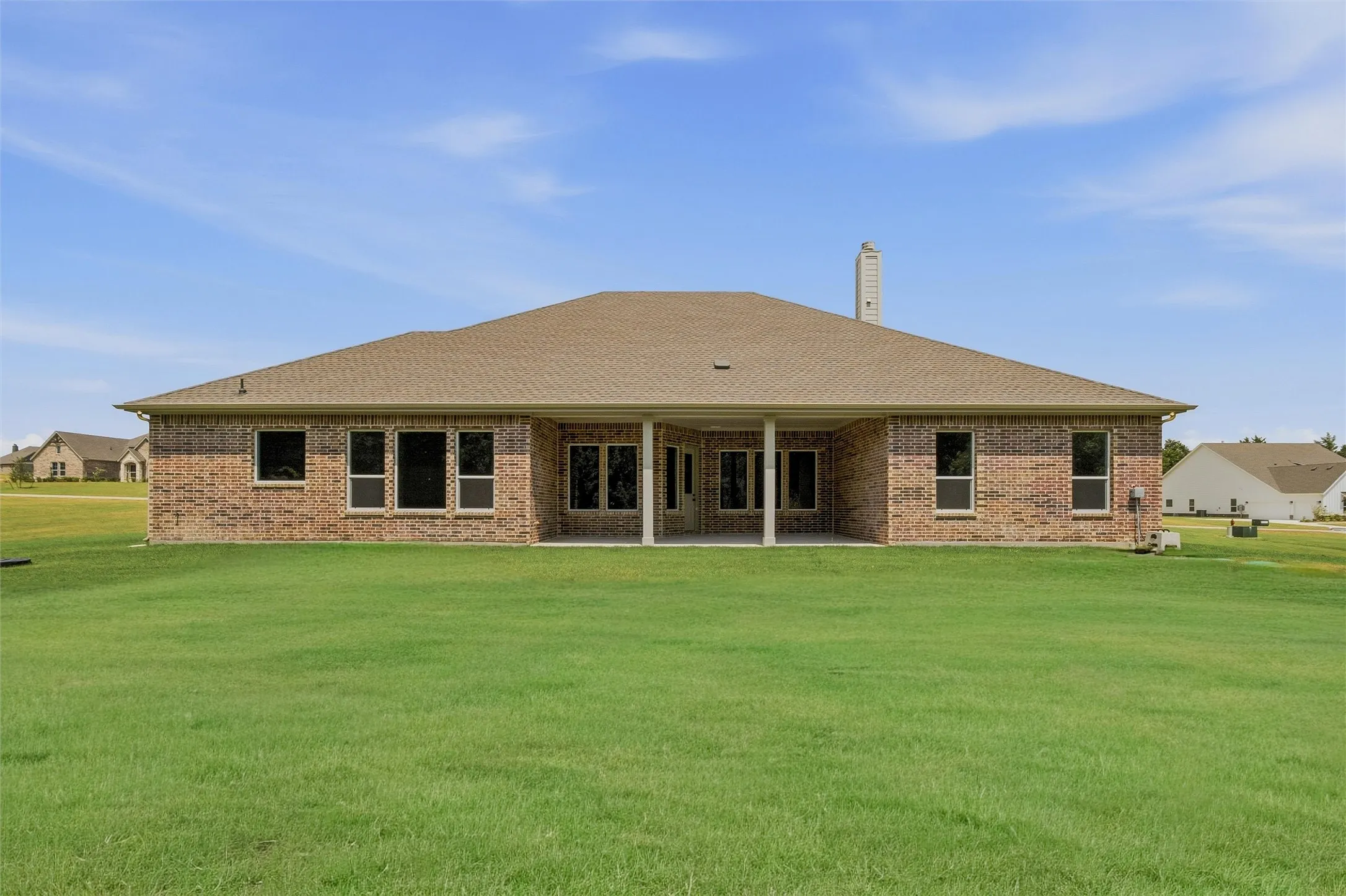 Brick exterior with multiple windows, covered patio, and a shingled roof
