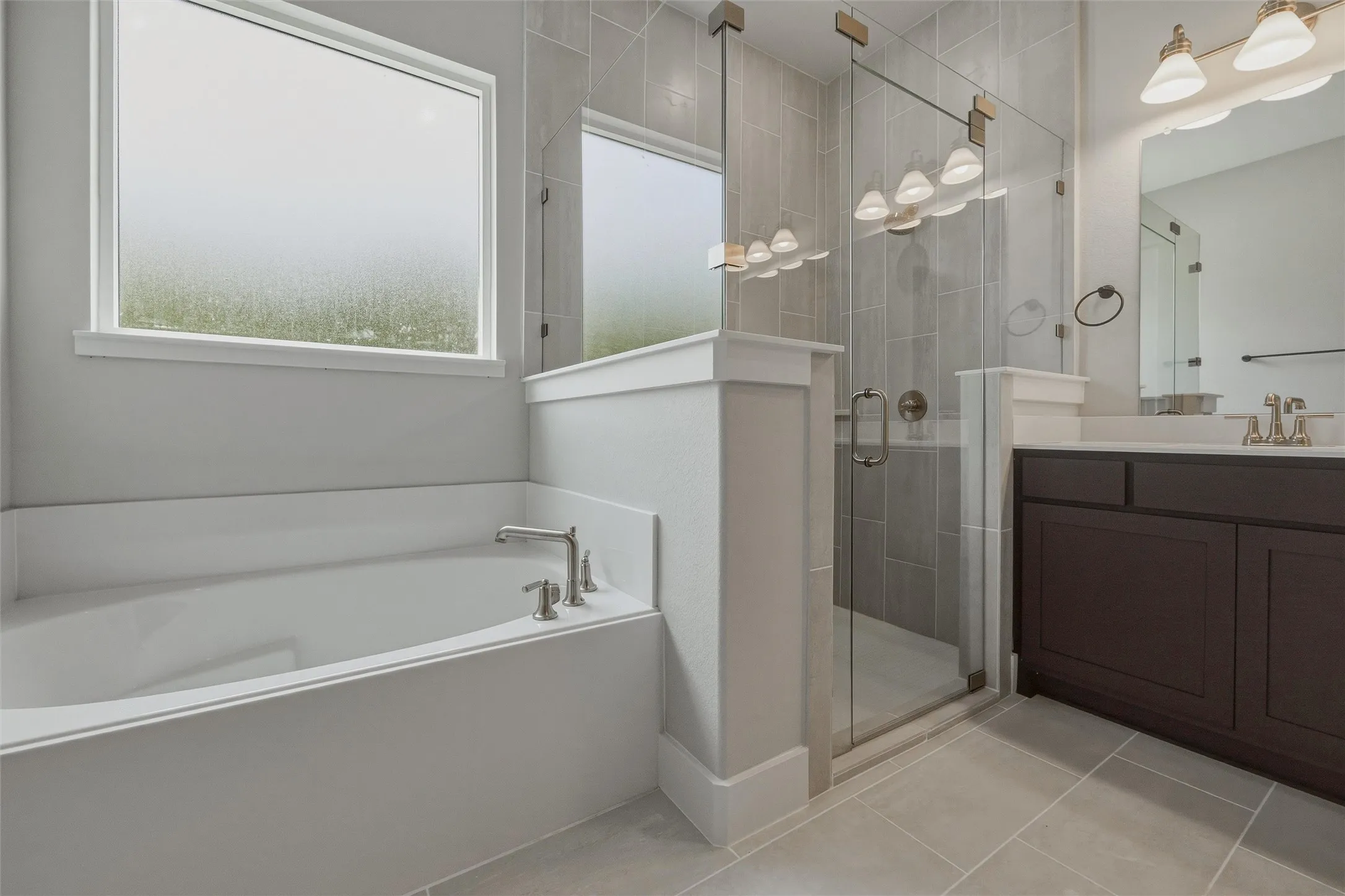 Built-in bathtub with polished chrome fixtures, glass-enclosed shower with tile surround, dark wood-finish vanity with countertop, and rectangular wall-mounted mirror