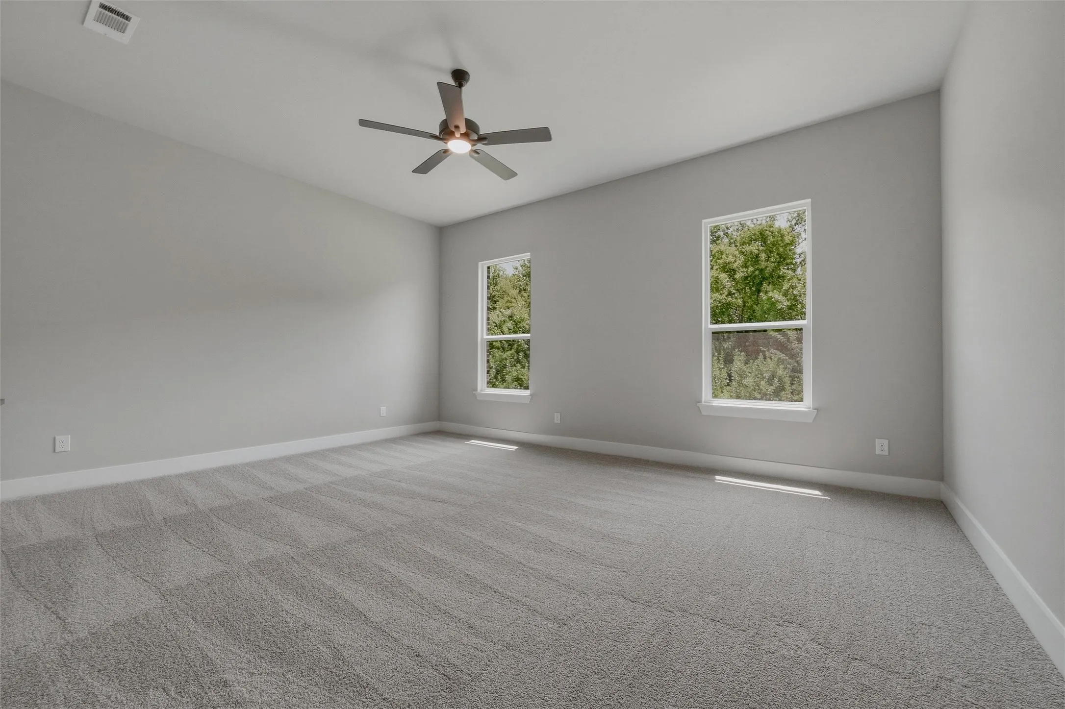 Spacious room featuring carpeting, two large windows, a ceiling fan, and sloped ceilings