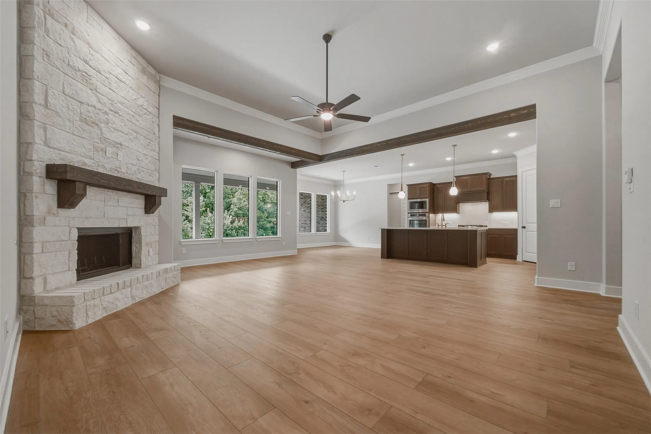 Wood-finish flooring, stone-clad fireplace with wood mantle, exposed wood beams, ceiling fan, and recessed lighting